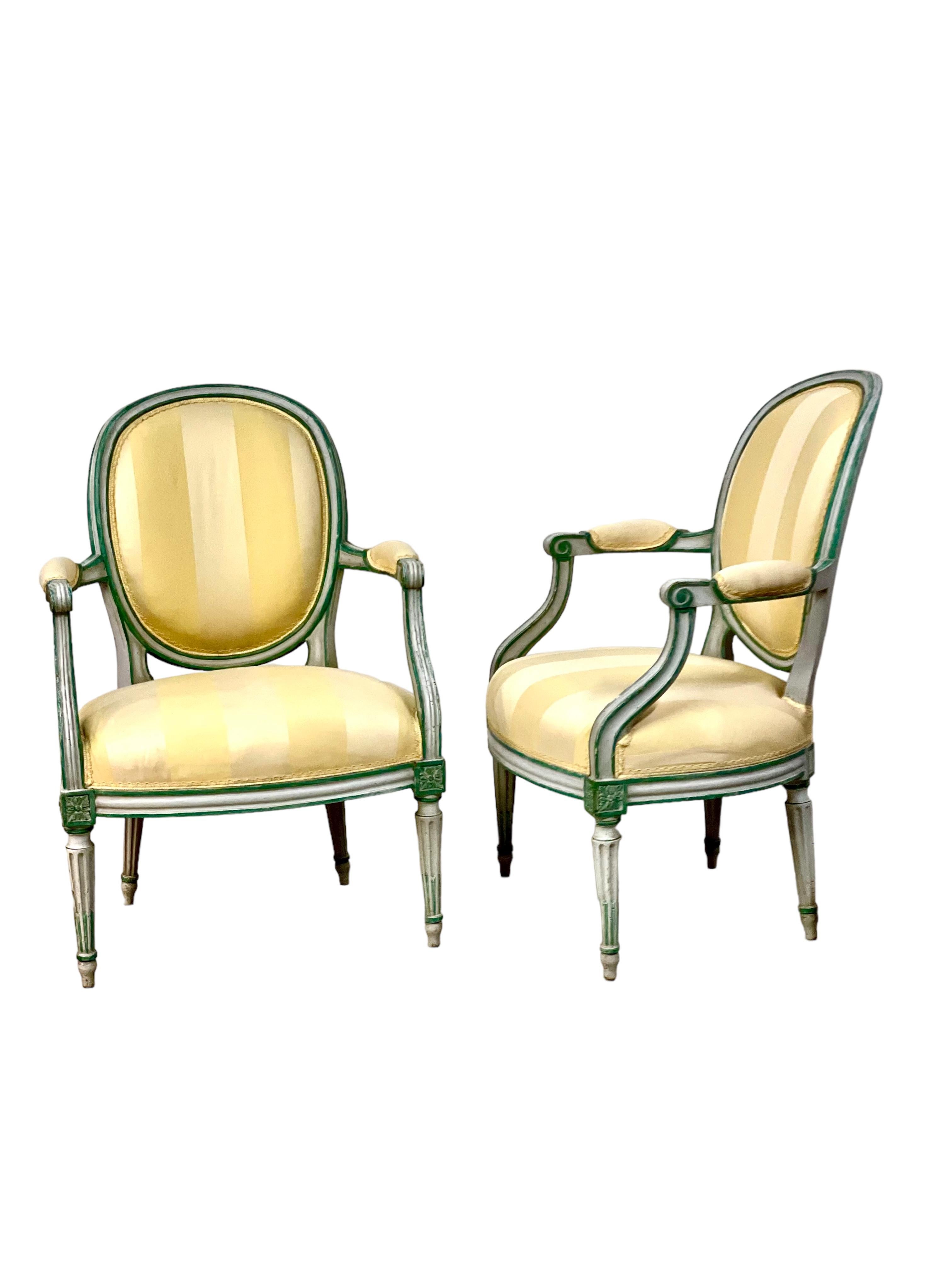 A charming pair of Louis XVI era 'Fauteuils en Cabriole', upholstered in stripes of luxurious cream and gold satin silk, edged in gold-braid trim. Discovered in a Provençal mansion, these open armchairs feature medallion-shaped concave backs, which,