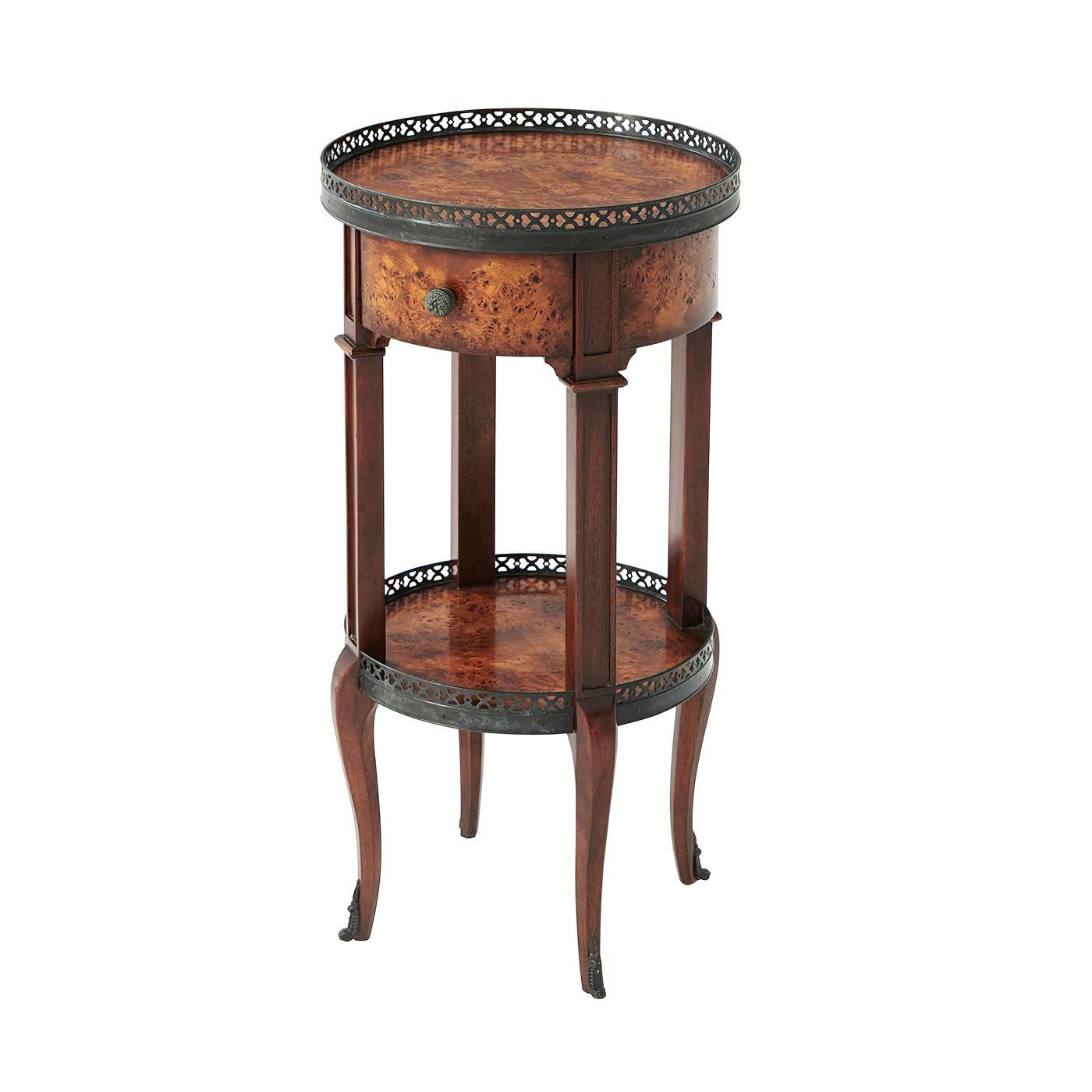 A French Louis XVI style round poplar burl side table, the burl veneer top with a patinated brass pierced gallery and similar under tier above a single bowed burl frieze drawer, square paneled supports on cabriole legs terminating in brass sabots.