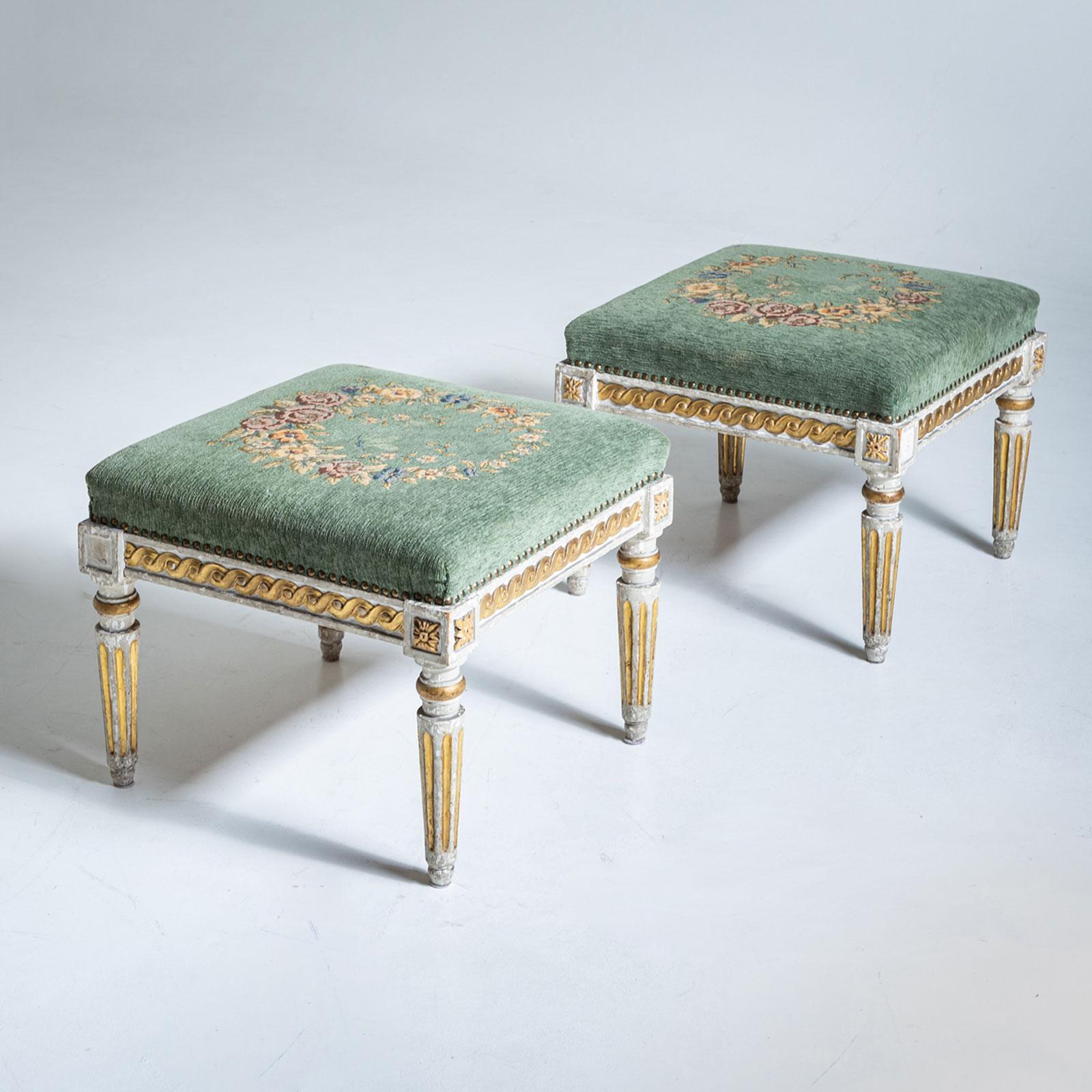 Pair of square stools with elegant tapered and fluted legs, accented by protruding corners and a delicate ribbon decoration on the apron. The seats are upholstered in green velvet, adorned with intricate floral wreath embroidery. The frame is