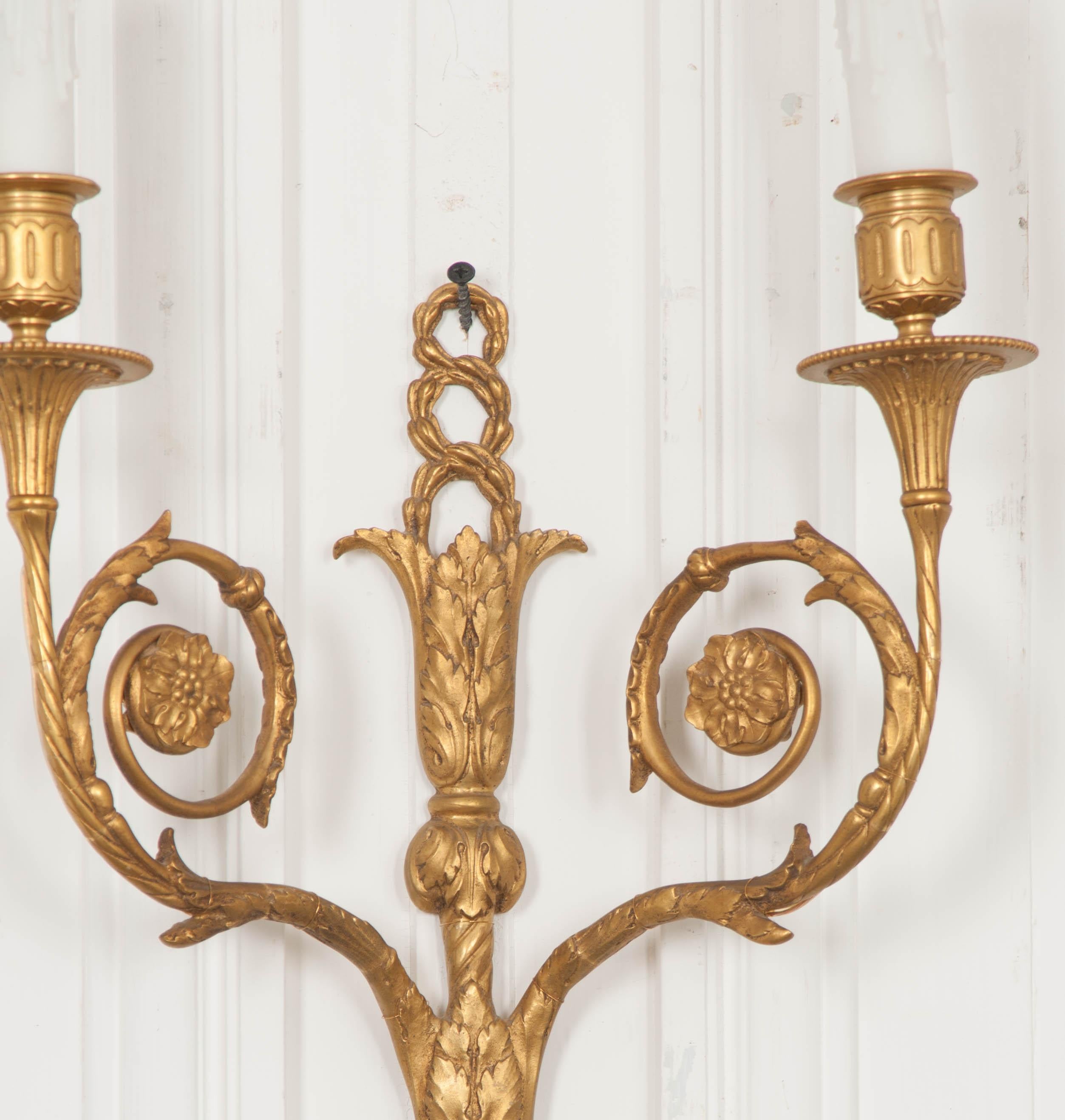 This fine pair of Louis XVI style gilt bronze two-light sconces, circa 1840, are from France and presented in the traditional laurel wreath, acanthus leaf, and rosette decor. Their patina is excellent and they will brighten up any room! Wired for