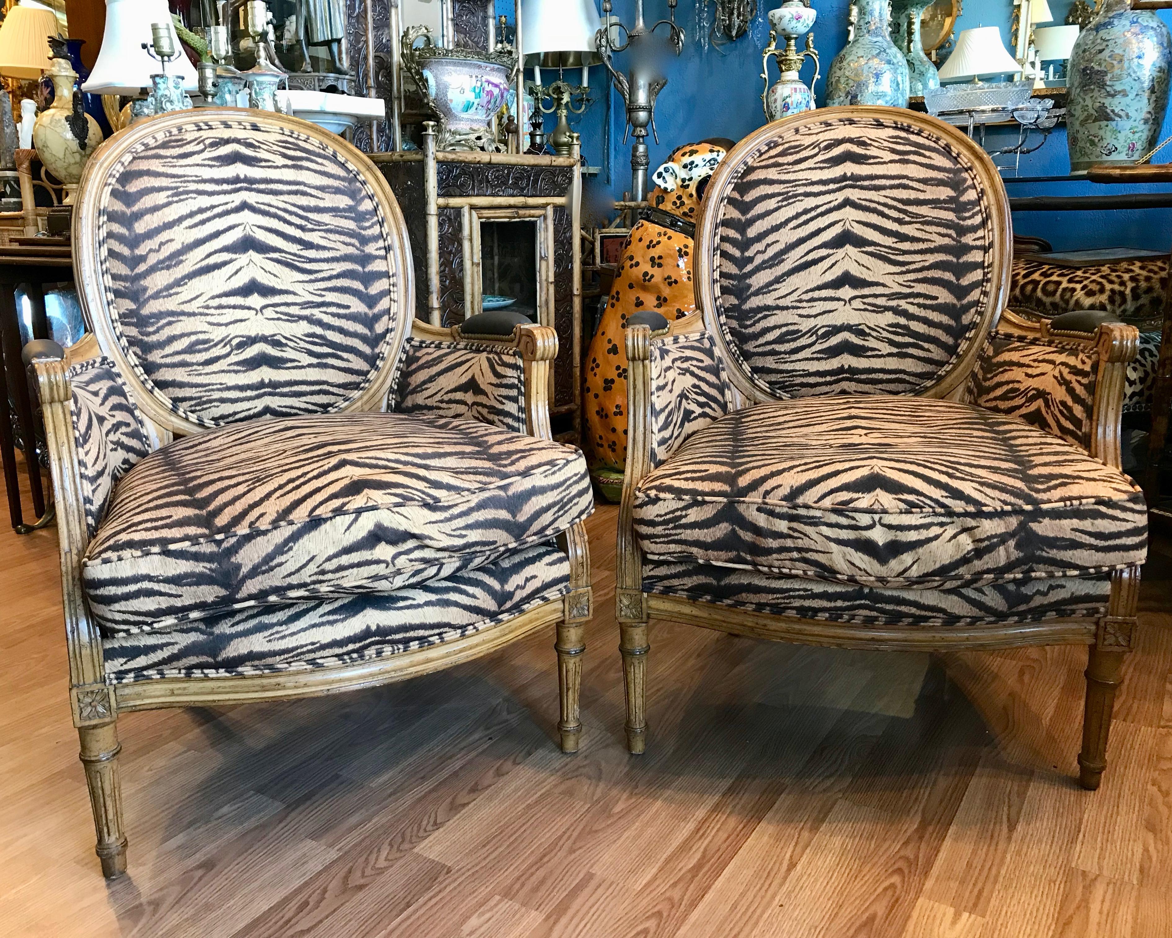 Beautifully fashioned with caned sides and appointed with faux tiger stripe fabric. This is a finely detailed pair with a nail head accented leather covered
arm rest and loose cushions 
A visually stunning pair of chairs