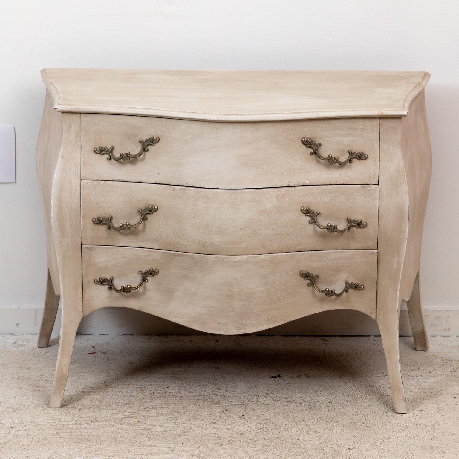 Circa 1920s pair of Louis XVI style grey painted three drawer bombe chests with lovely proportions and metal hardware. Please note of wear consistent with age including wear to paint on edges, scuff marks, and paper lining of drawers that show