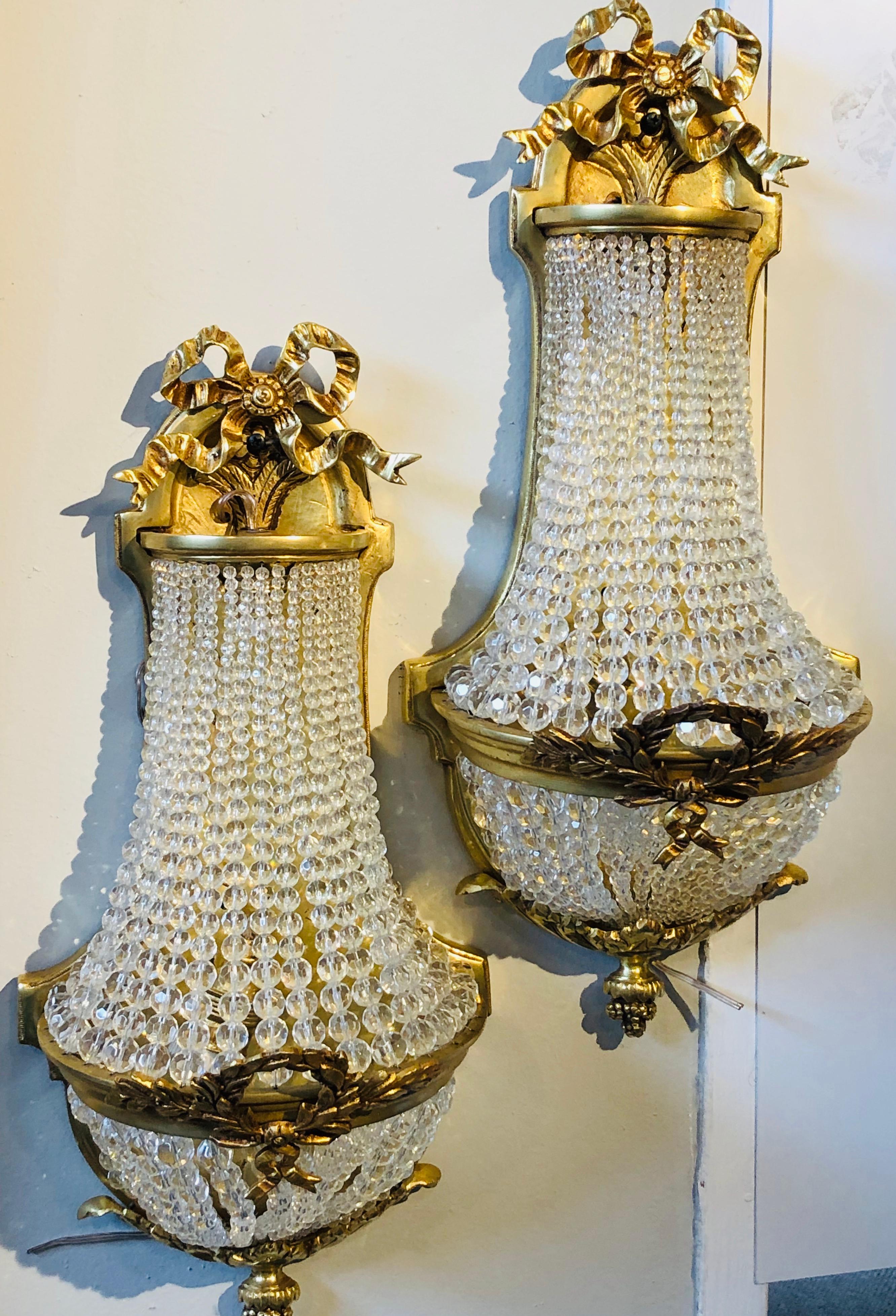 Pair of Louis XVI style bronze and crystal beaded diminutive wall sconce. This finely case pair of beaded wall sconce are certain to make a statement in any room in the home or office having a tassel and ribbon decorated frame with drapery crystal