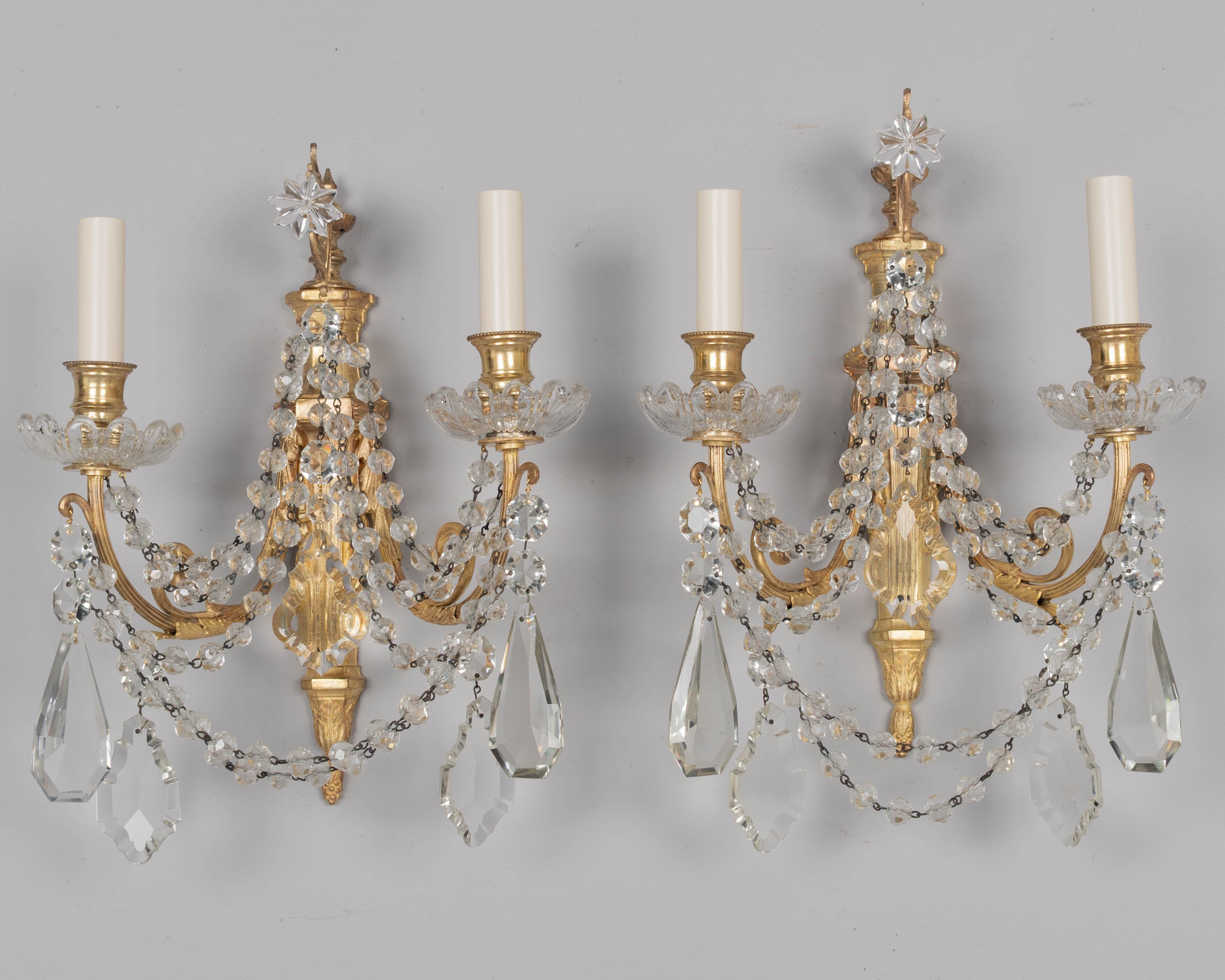 Coppia di appliques a due luci in bronzo fuso in stile Luigi XVI con bracci a voluta e una varietà di prismi e pendoli in cristallo e catene di perline sfaccettate. Un buon getto pesante. Ricablato con nuove prese e copricandela. Una bobeche è