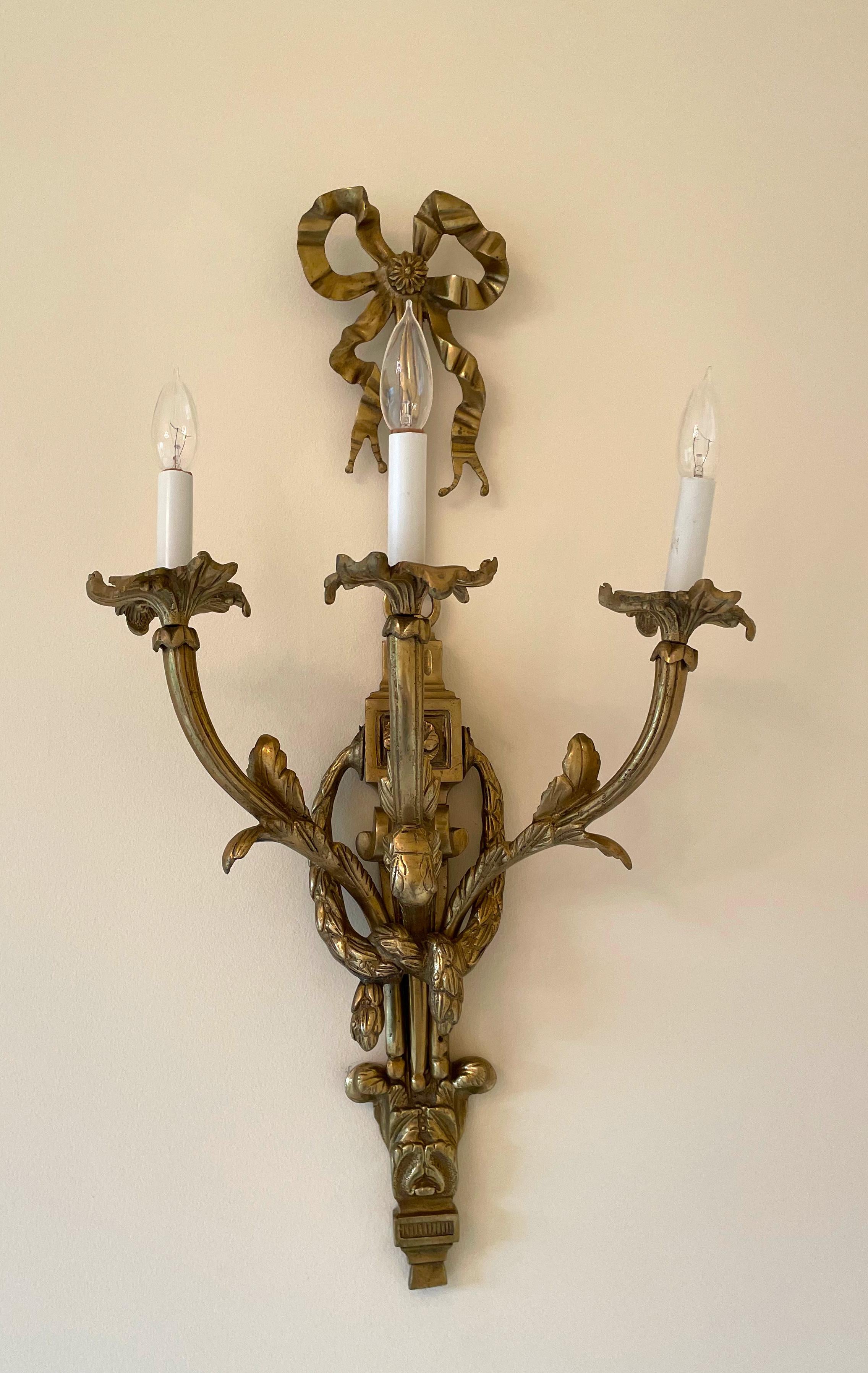 
Zwei Wandleuchten im Louis XVI-Stil aus Bronze
Die Rückenplatte ist in Form von Schleifenbändern gegossen, die verschnörkelte Arme tragen. 
800 Höhe 81,28 cm (32 in.), Breite 38,1 cm (15 in.), Tiefe 20,32 cm (8 in.) (ungefähr)
