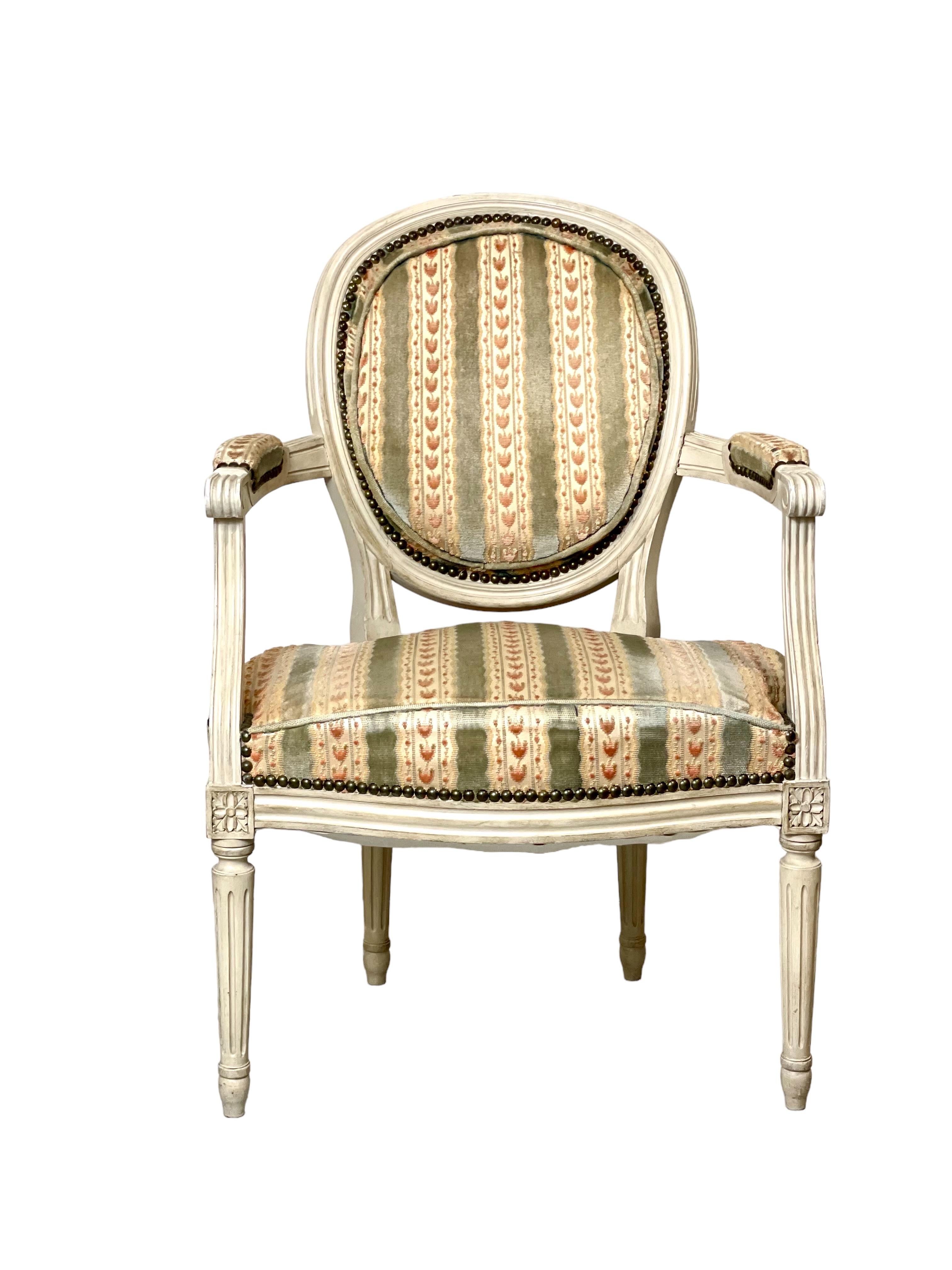 Magnifique paire de fauteuils 'Fauteuil Cabriolet' de style Louis XVI à dossier médaillon, en bois laqué blanc. Les accoudoirs sont partiellement rembourrés et cannelés, et chaque chaise repose sur quatre élégants pieds cannelés avec des rosettes