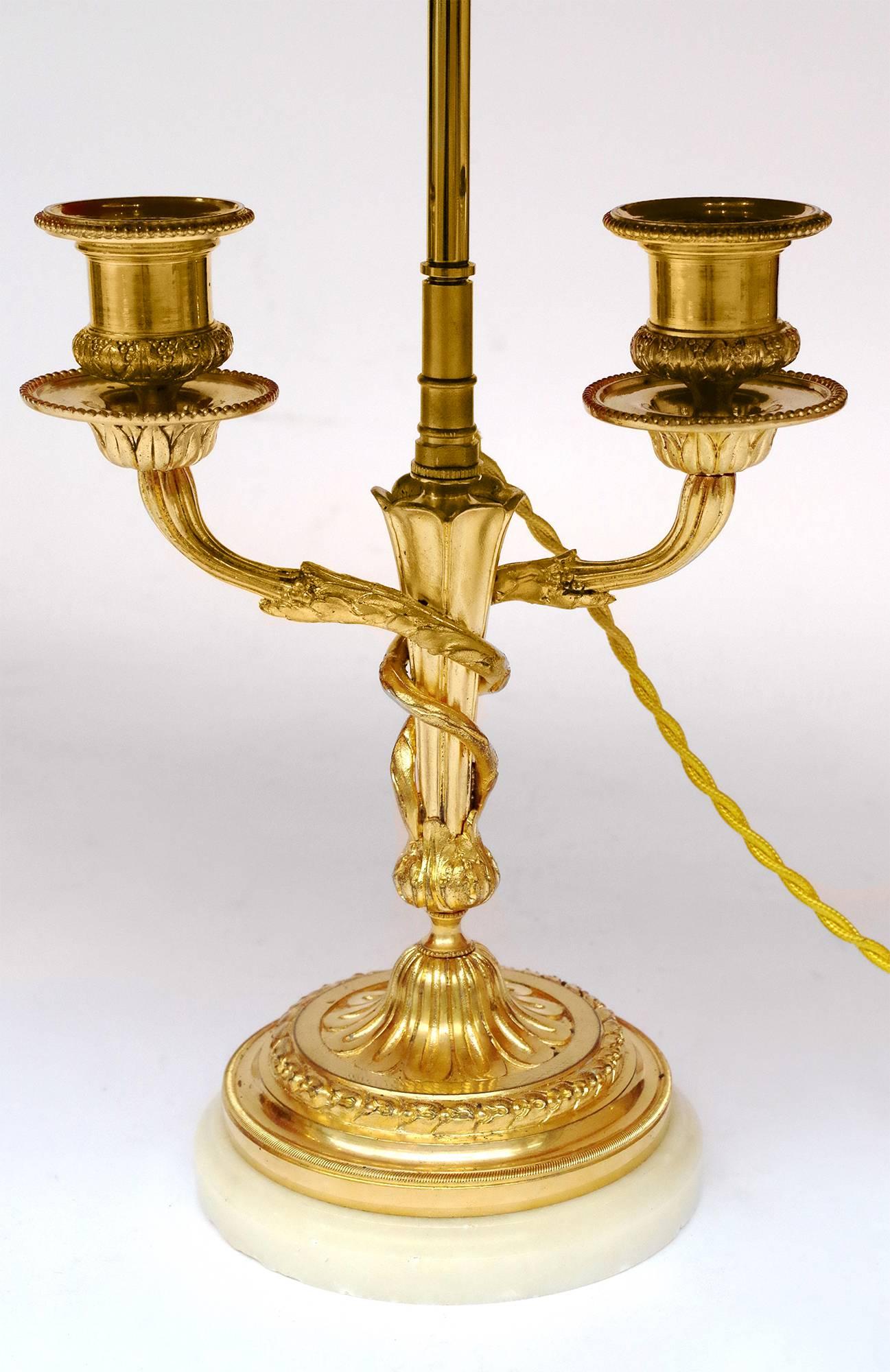 Pair of two Louis XVI style candlesticks in chiselled and gilt bronze mounted in lamps. Circular stand in Carrara white marble topped by a laurel wreath and a gadroon base. Around the torch shape shaft two plant branches are interlaced and end in