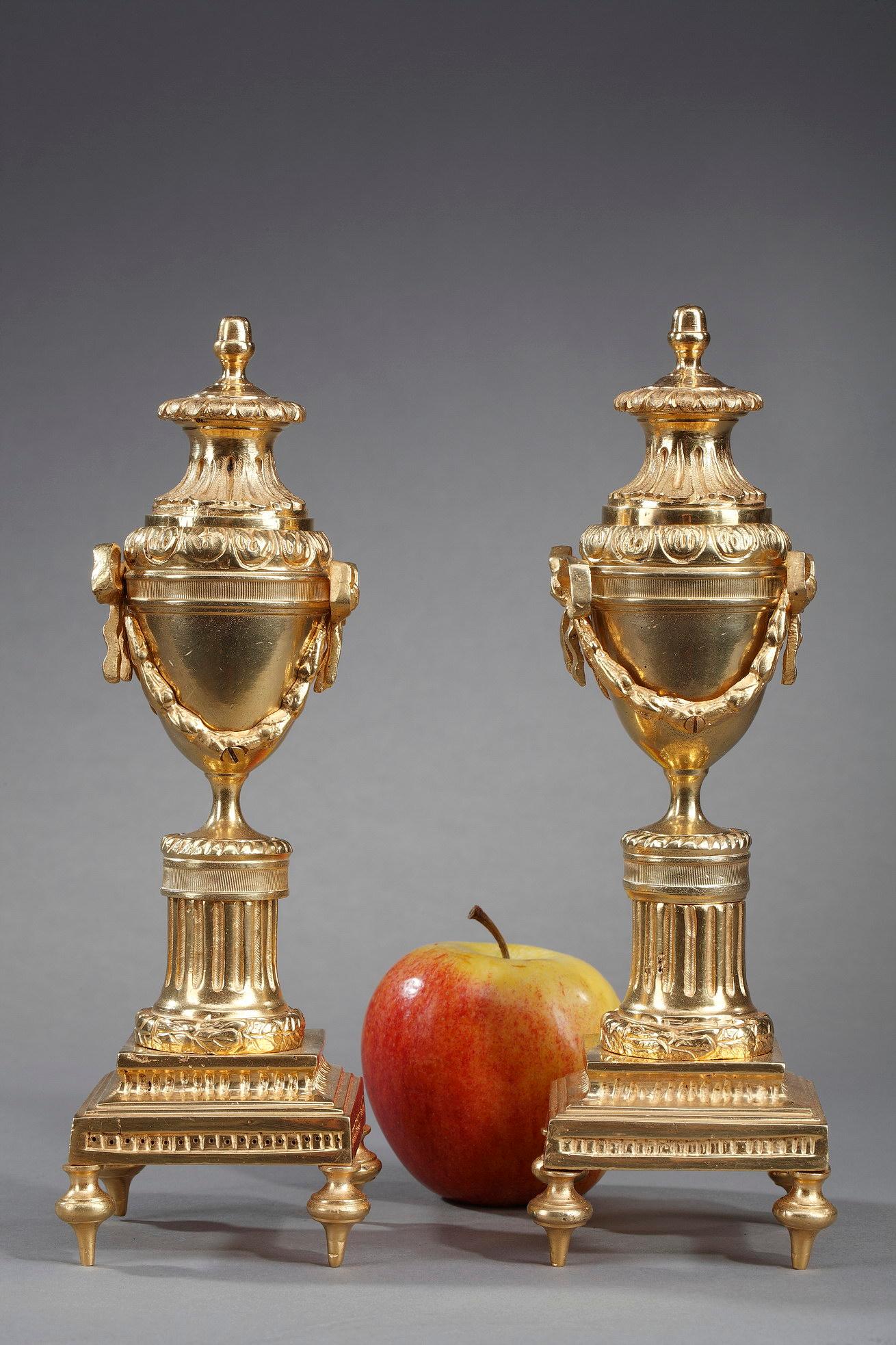 Pair of small Louis XVI style cassolettes in gilt bronze acting both as torches and urns. The urns are decorated with garlands of laurels and rests on a fluted column. The lid of the cassolette is reversible: one side serves as a candle holder and