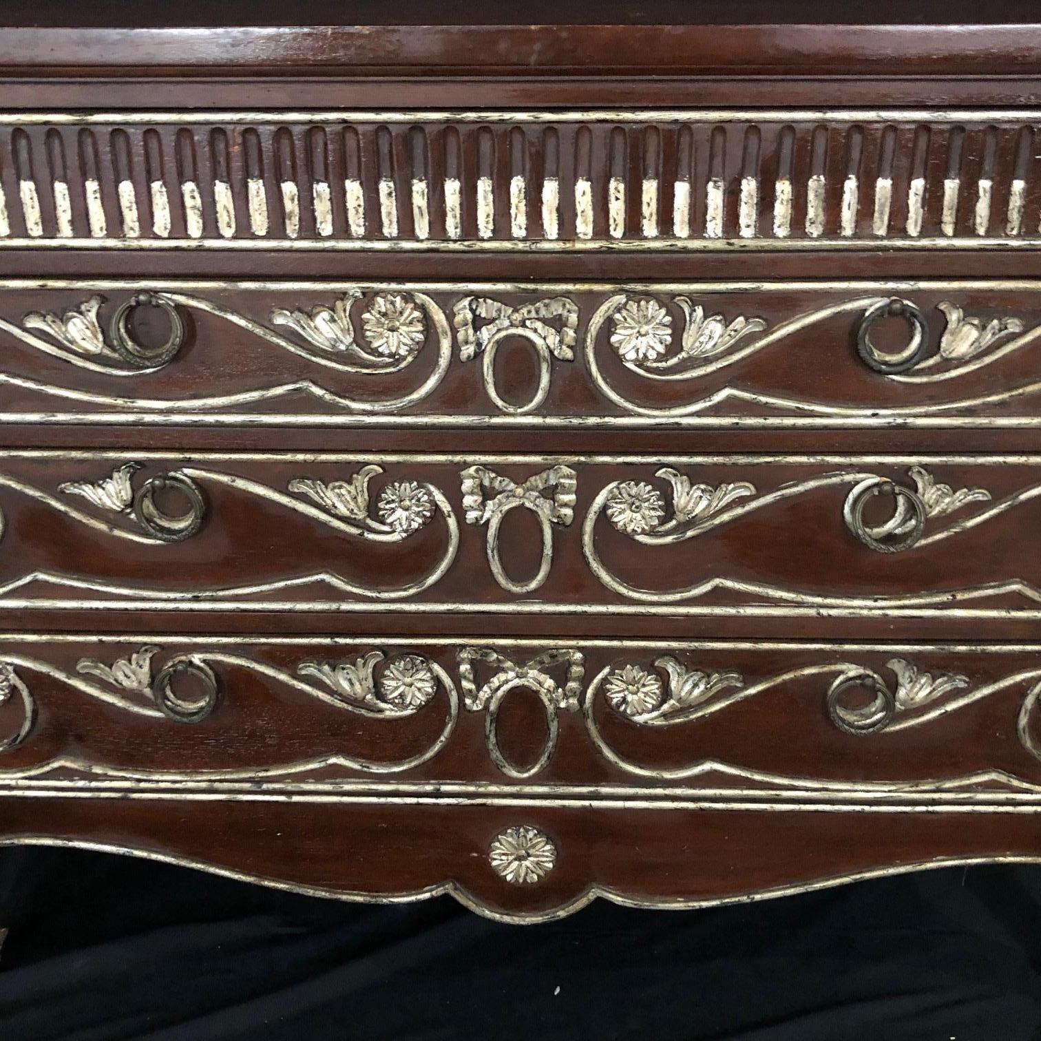 Pair of Louis XVI style mahogany chests of drawers with beautiful and dramatic silver gilt accents. Three drawers in each commode with silver pulls provide ample storage; reeded sides are capped with silver florets, all-over tapering reeded feet