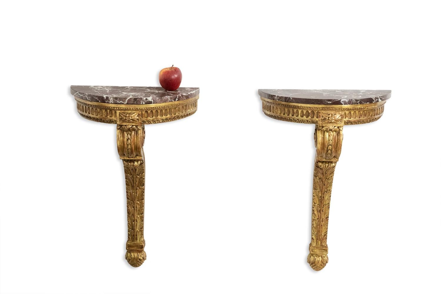 Pair of Louis XVI style consoles from the Napoleon III period, half-moon shaped, with their morello cherry marble tops, the base in carved and gilded wood with leaf decoration of scrolls, or waves, in the central part at decorated with large oak