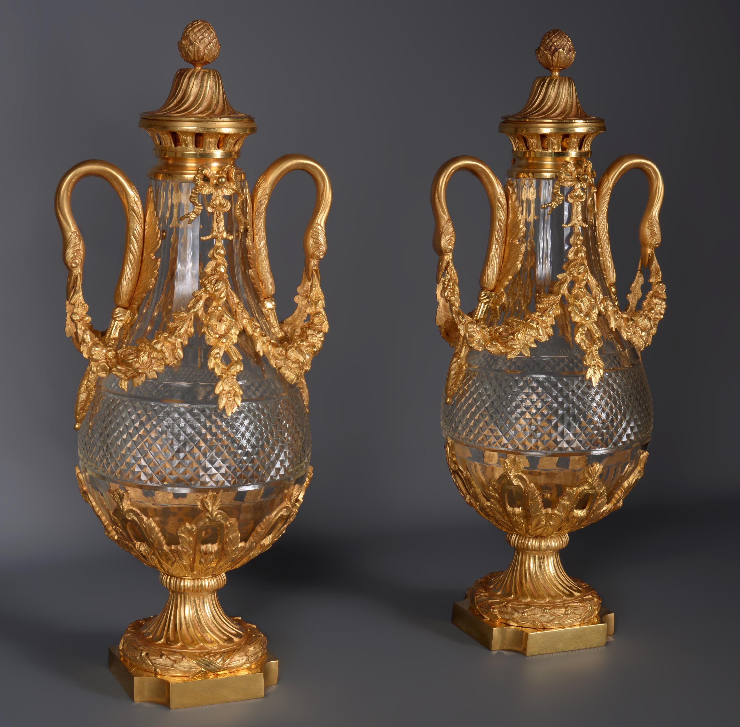 Cette élégante paire de vases en cristal taillé est ornée d'une délicate monture en bronze doré. 
Les anses représentant des cygnes tiennent une guirlande de fleurs. Les deux ont leur couvercle d'origine.