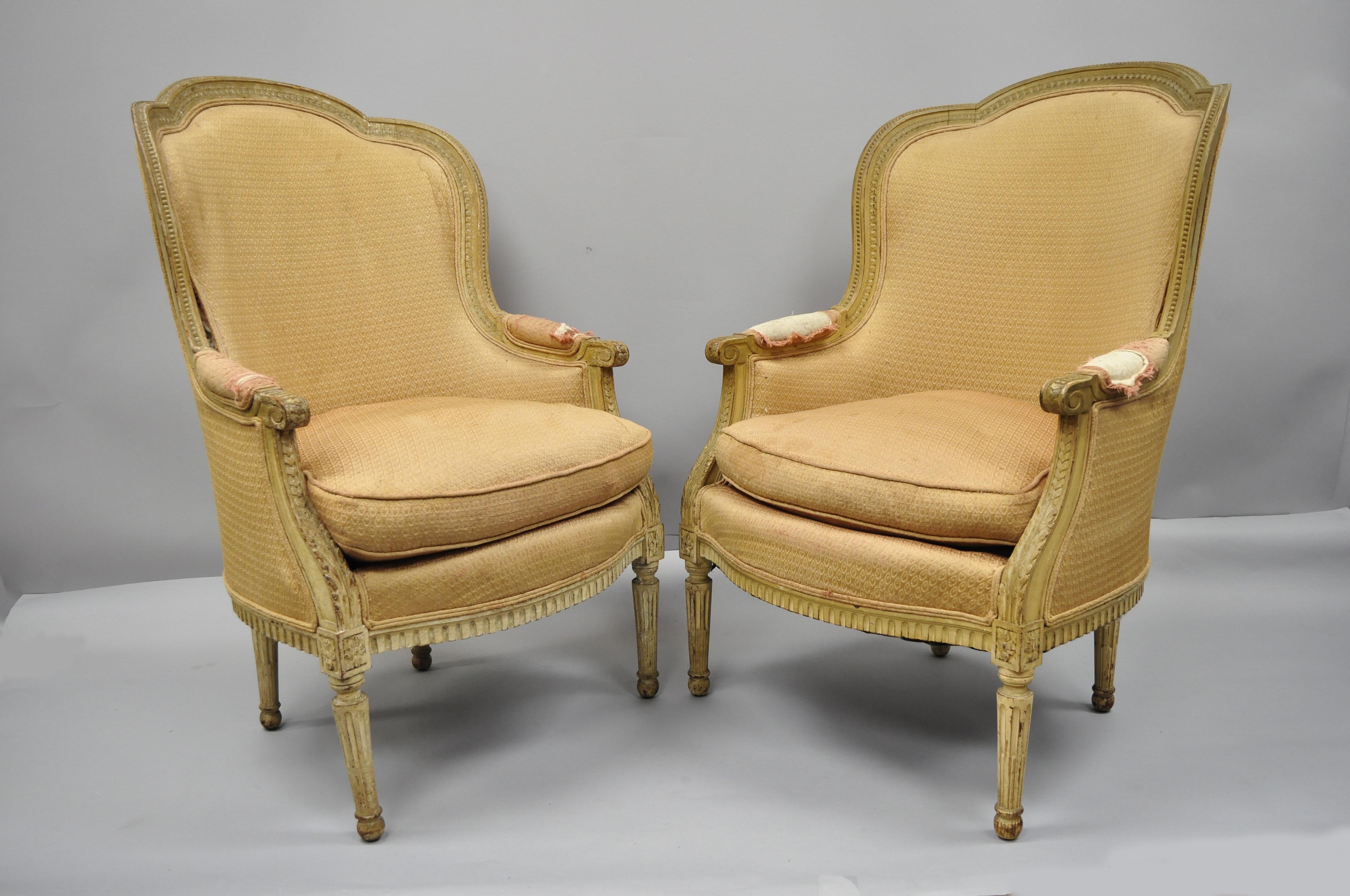 Pair of French Louis XVI style distress painted bergère armchairs attributed to Maison Jansen. Item features remarkable distress painted cream finish, finely carved frame, reeded and tapered legs, shaped top rail, barrel back, authentic aged patina,