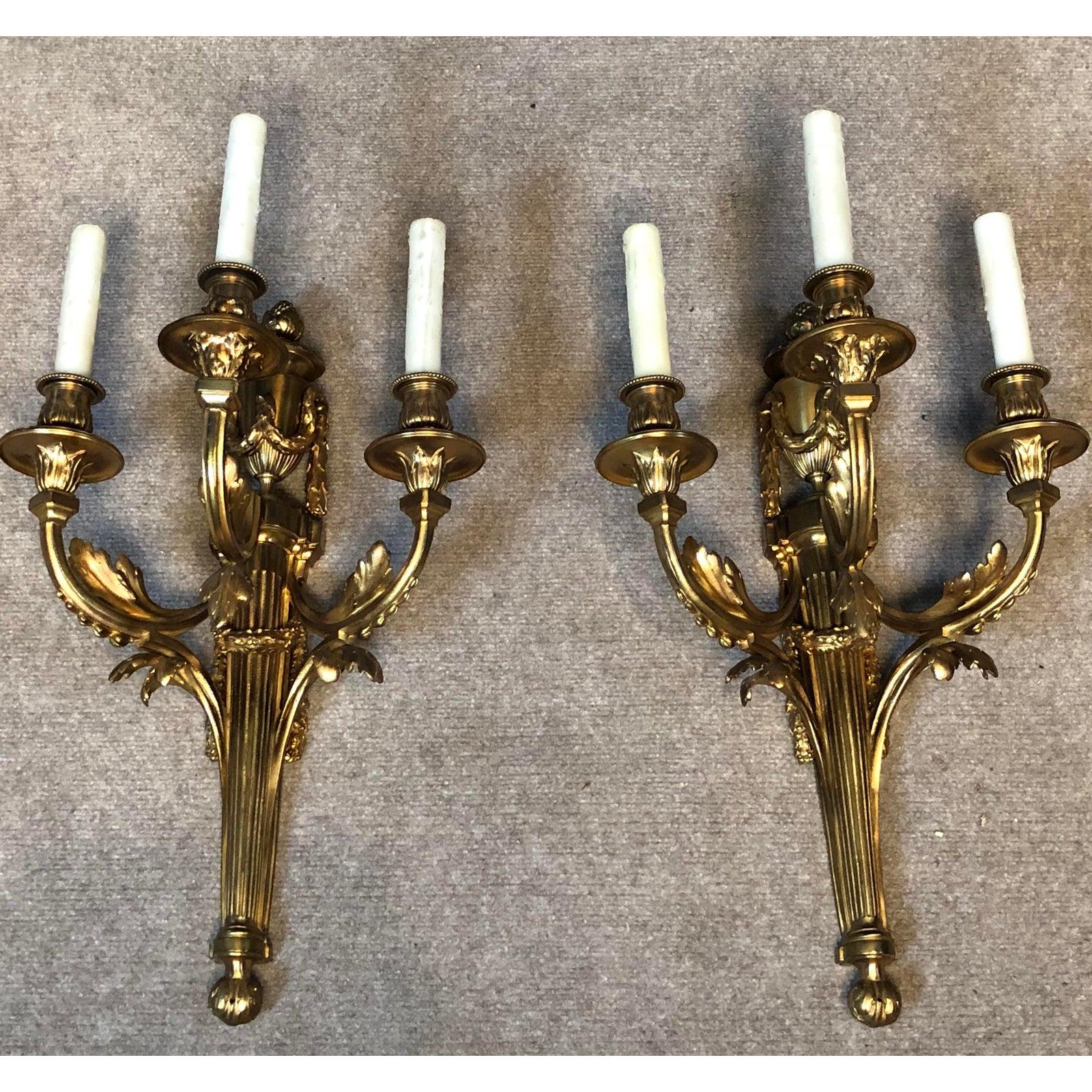 Pair of Louis XVI three arm gilt bronze wall sconces. French, 19th century. Fine quality bronze work. Urn and garland form top. Wired