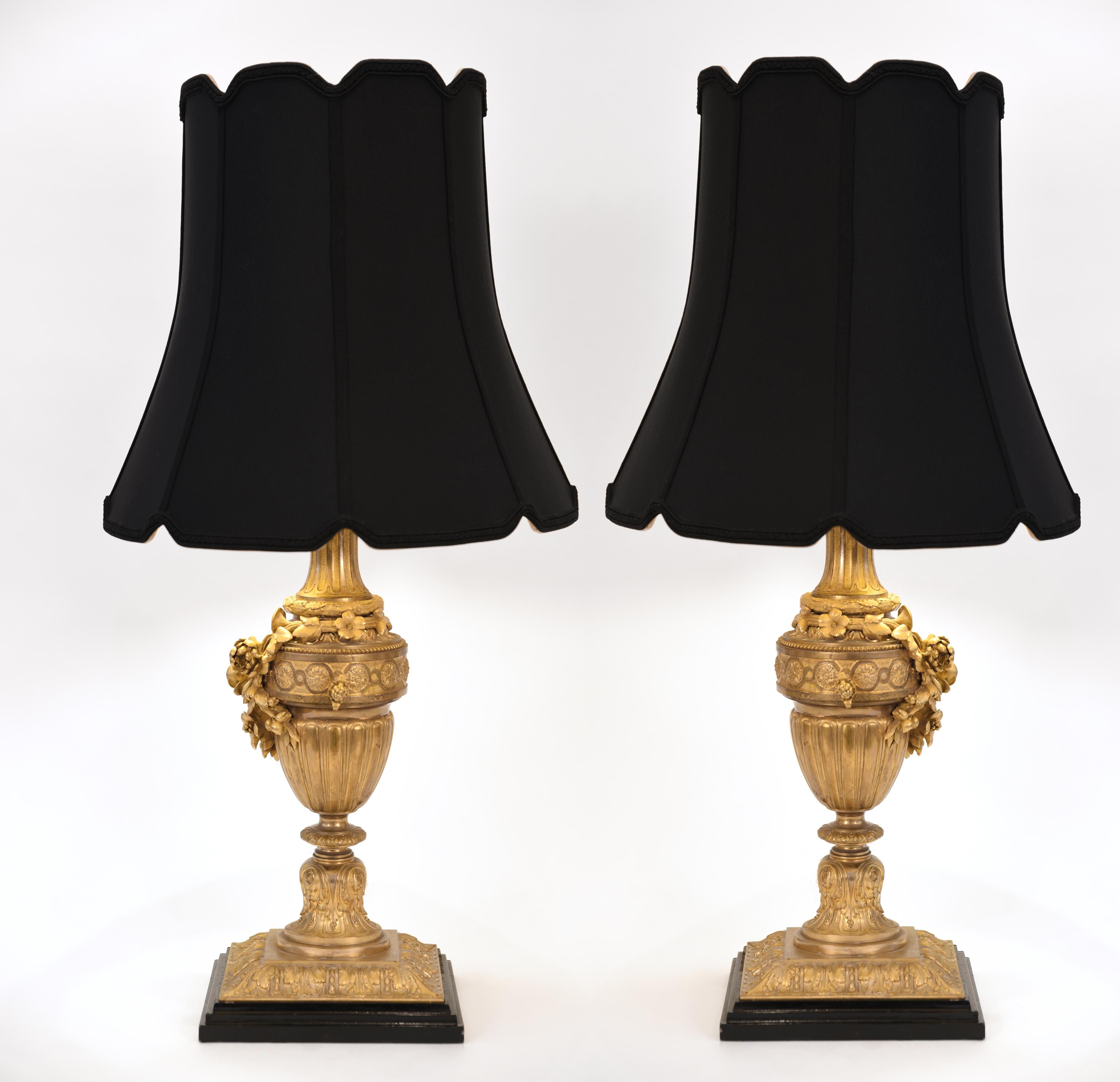 A pair of Louis XVI style gilt bronze task / table lamps. Each lamp is in excellent antique working condition, rewired for US use. Each lamp comes with a white round drum with silk exterior shade measuring 13 inches x 14 inches x 13.5 inches. Each