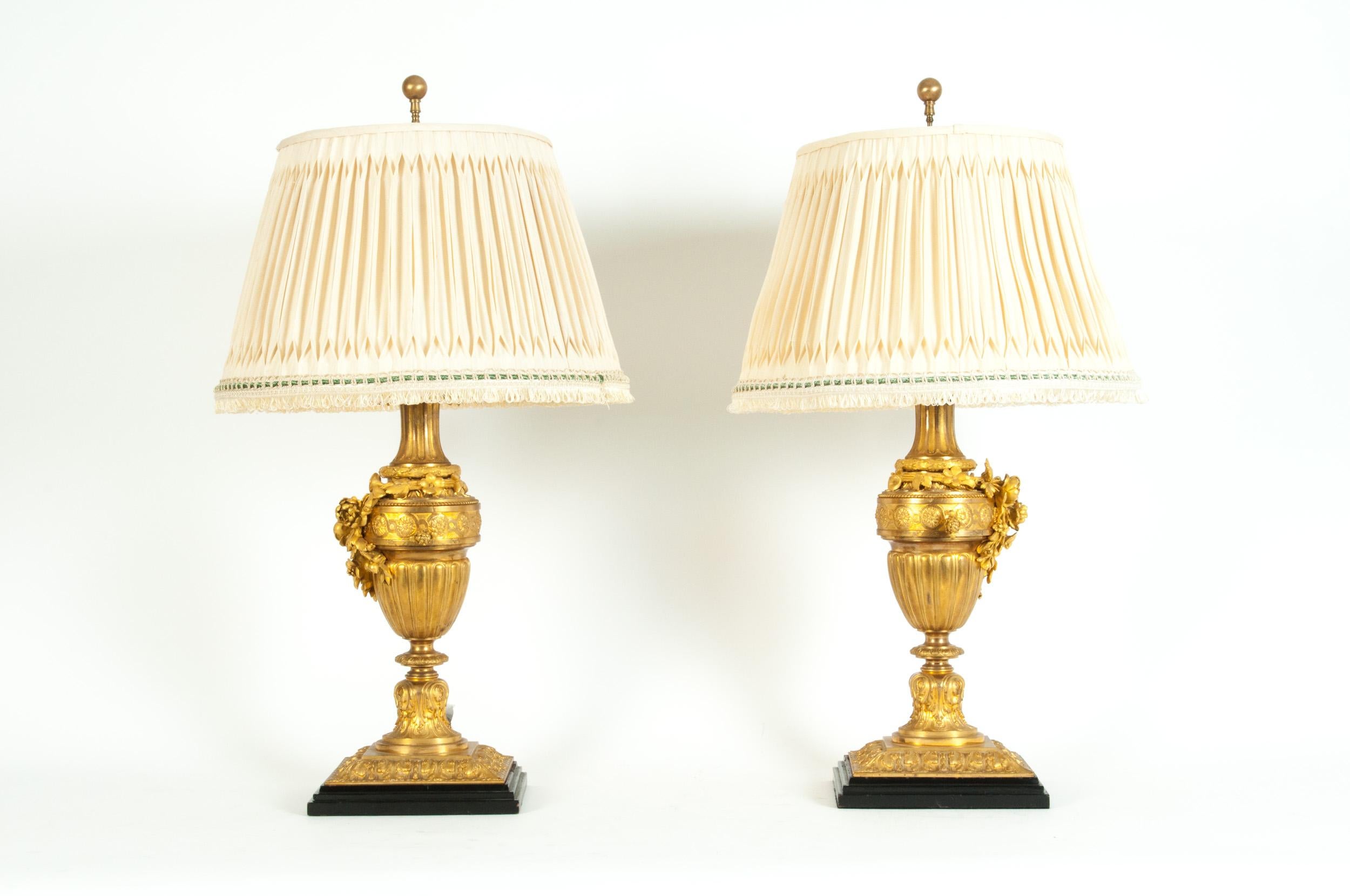 A pair of Louis XVI style gilt bronze task / table lamps. Each lamp is in excellent antique working condition, rewired for US use. Each lamp comes with a round pleated silk shade measuring 11 inches long x 17 inches base diameter. Each lamp measure