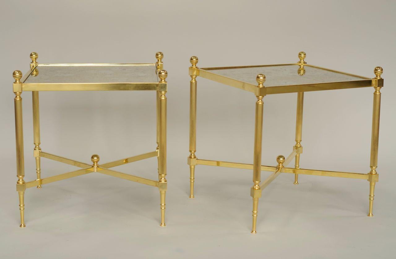 Pair of gilt brass Louis XVI style side tables. The oxidized mirror top stands on a gilt brass structure with fluted legs, linked by an X-shaped strut.
Work from the 1970s.