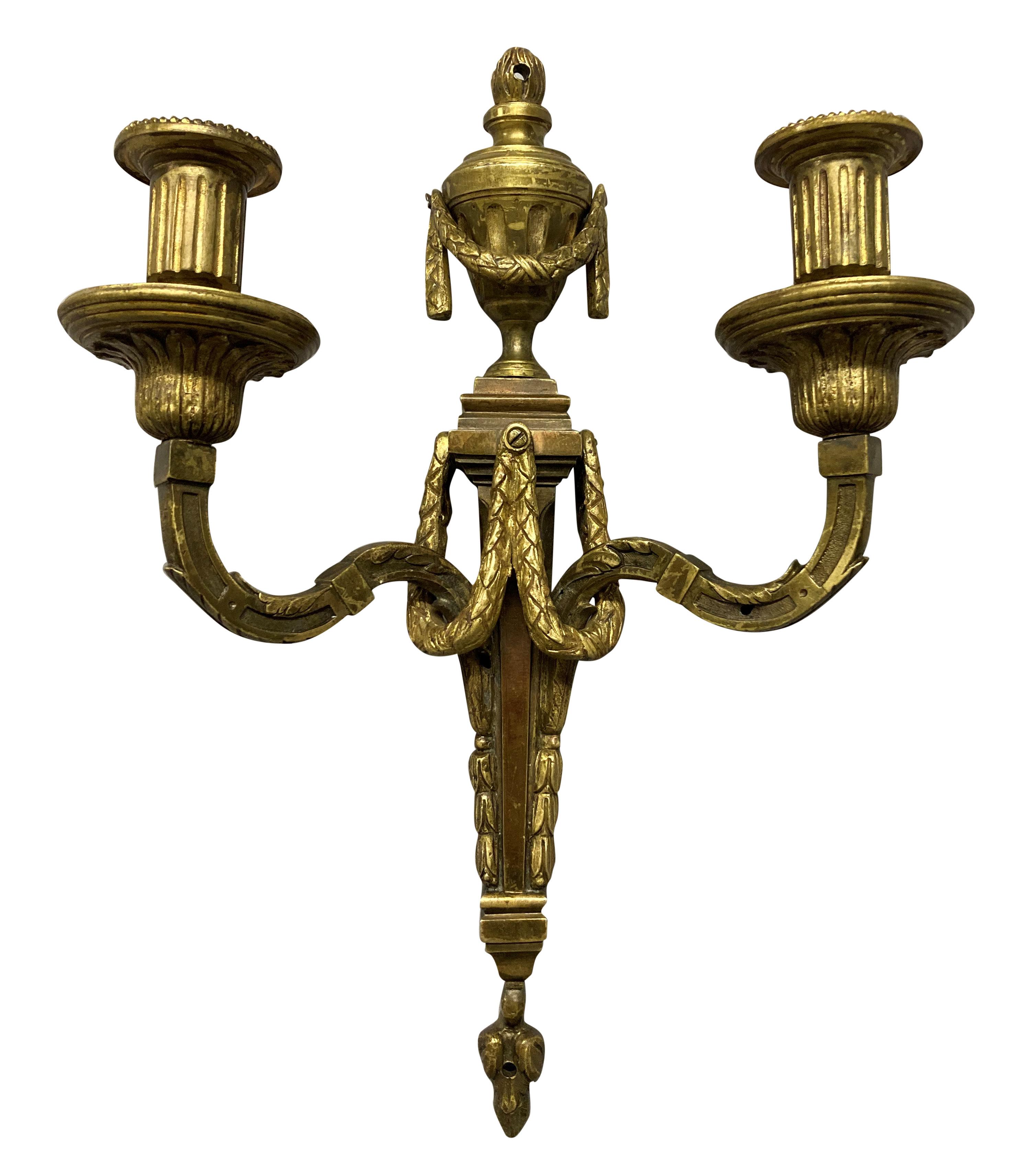 A pair of French Louis XVI style twin branch gilt bronze wall sconces, depicting urns and swags.