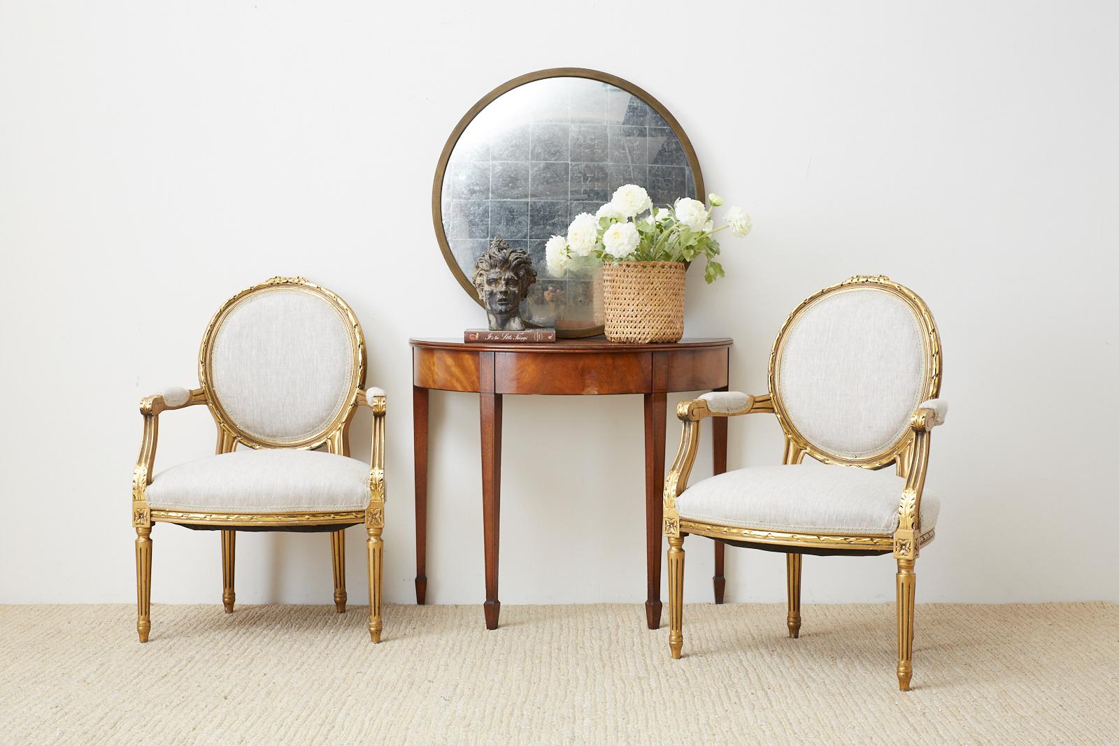 Lavish pair of French giltwood fauteuil armchairs hand carved in the Louis XVI taste. The beautiful frames have a round back and feature a new organic linen upholstery. The seats are embellished with decorative rosettes on the corners and they are