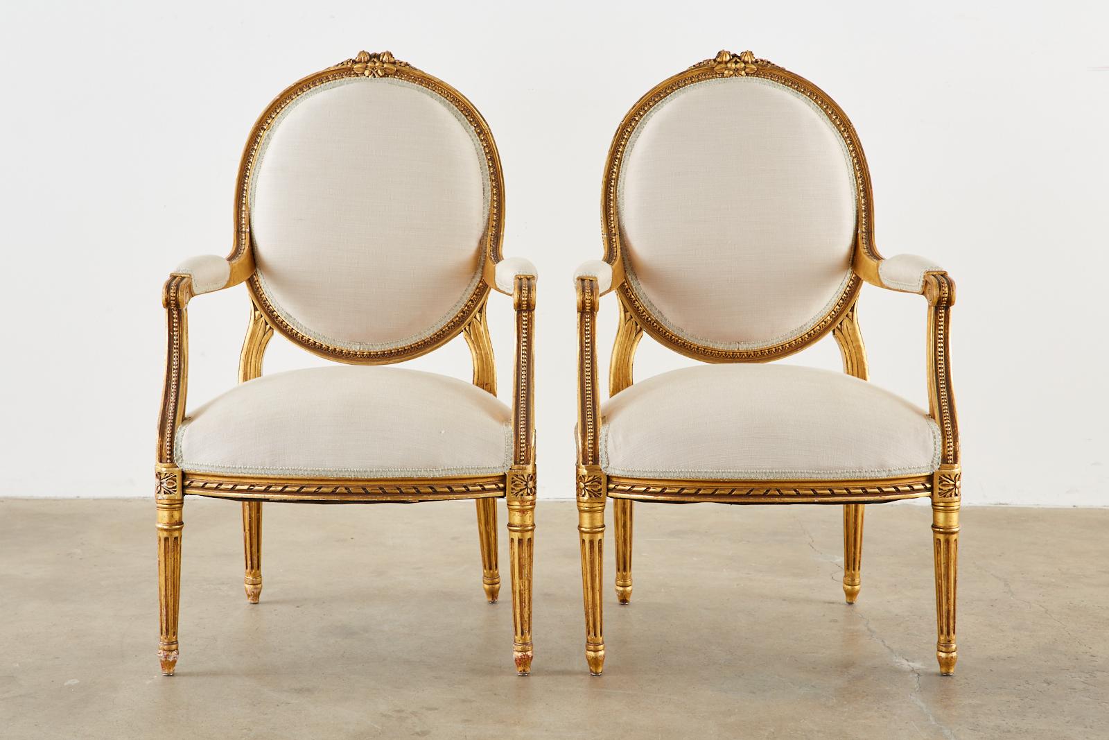 Stunning pair of late 19th century French fauteuil armchairs made in the grand Louis XVI taste. The chairs feature fine, highly carved giltwood frames embellished with rope, bead, and rosette decoration and topped with floral ribbon crests on the