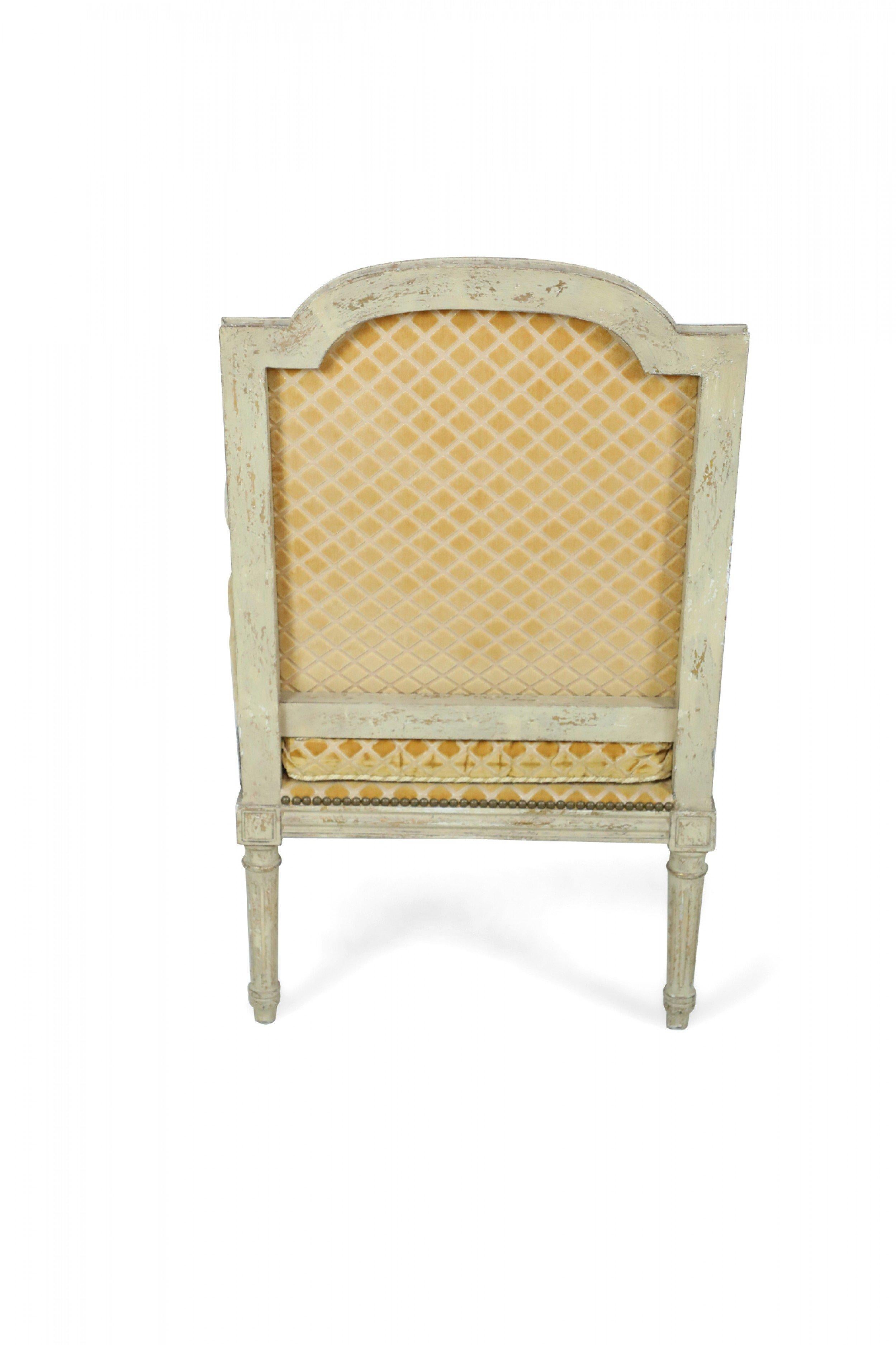 Pair of Louis XVI-style (19/20th Century) fauteuils / armchairs with distressed grey painted frames on turned fluted legs having a gold diamond-patterned upholstery on seats, backs, and arm rests with decorative metal nail heads (priced as pair).
 