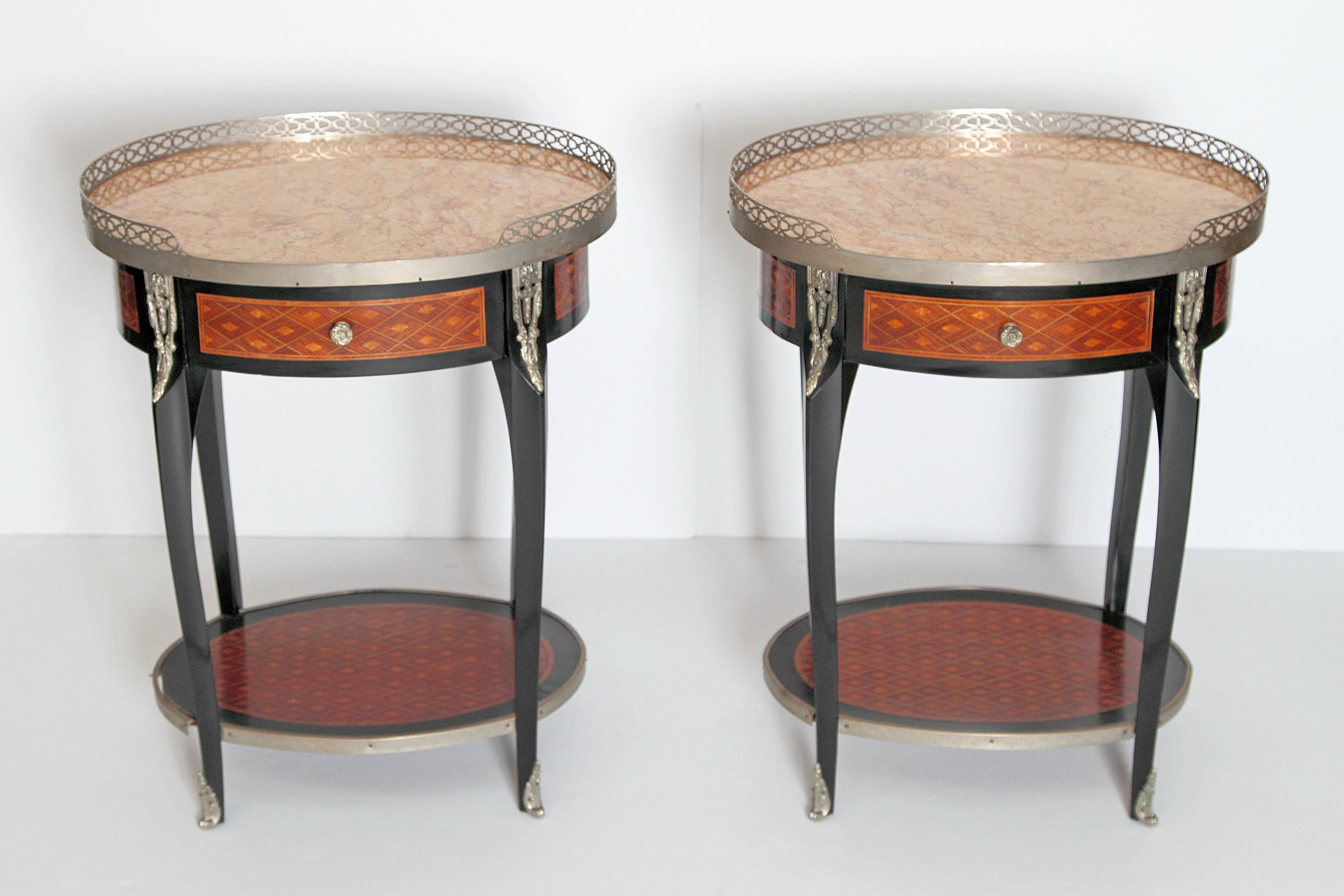 A pair of French Louis XVI-style oval guéridons, occasional or side tables with peach colored stone tops. Silver gilt gallery around top with other silver gilt bronze decorative mounts. Each with single drawer, apron, and lower shelf decorated in an