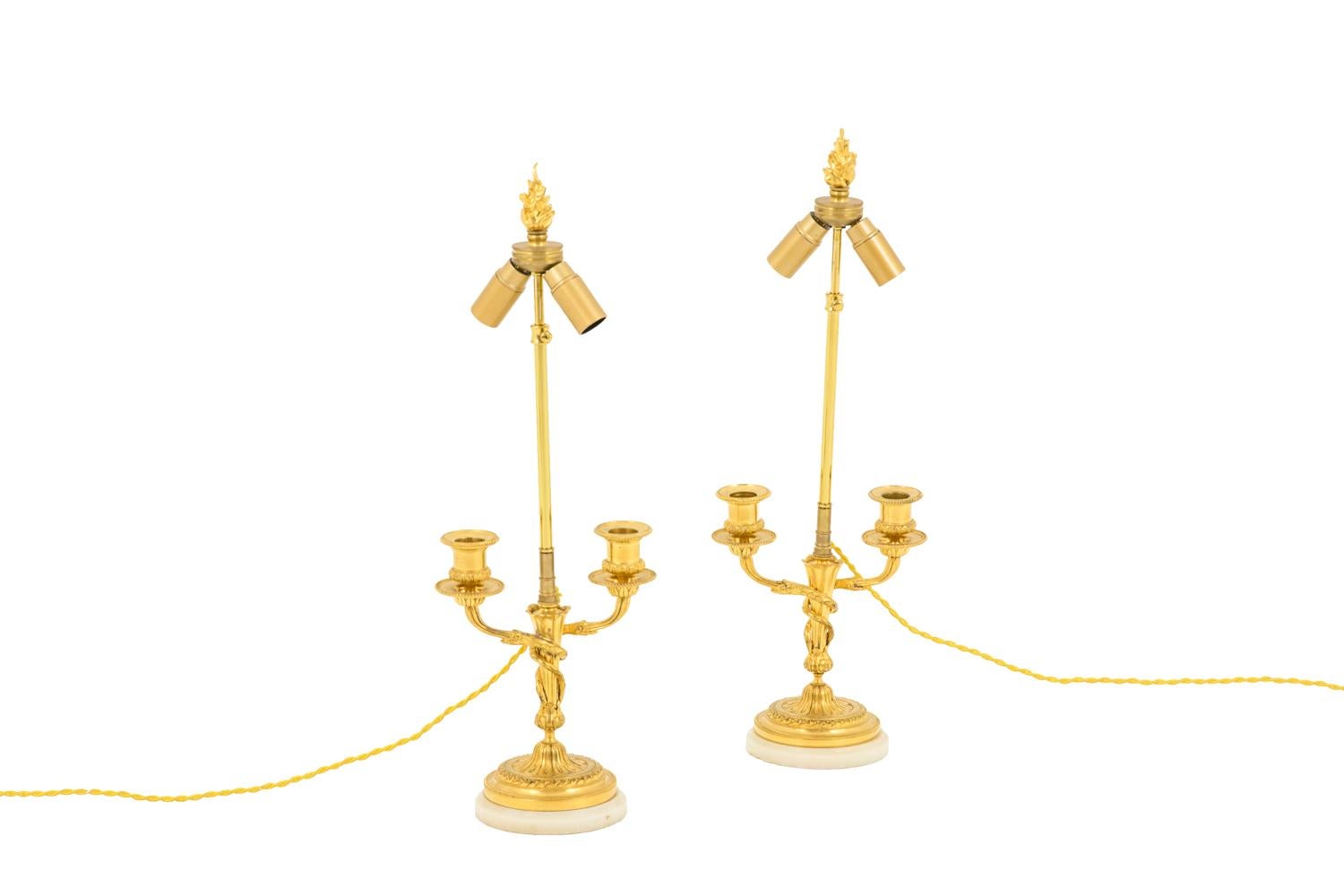 Pair of Louis XVI style lamps in gilt bronze with two acanthus leaves shaped fires wrapped around the shaft. Two arm lights with bobeches decorated with a beads frieze and grapes and cups adorned with a beads frieze and water leaves. Flared shaped