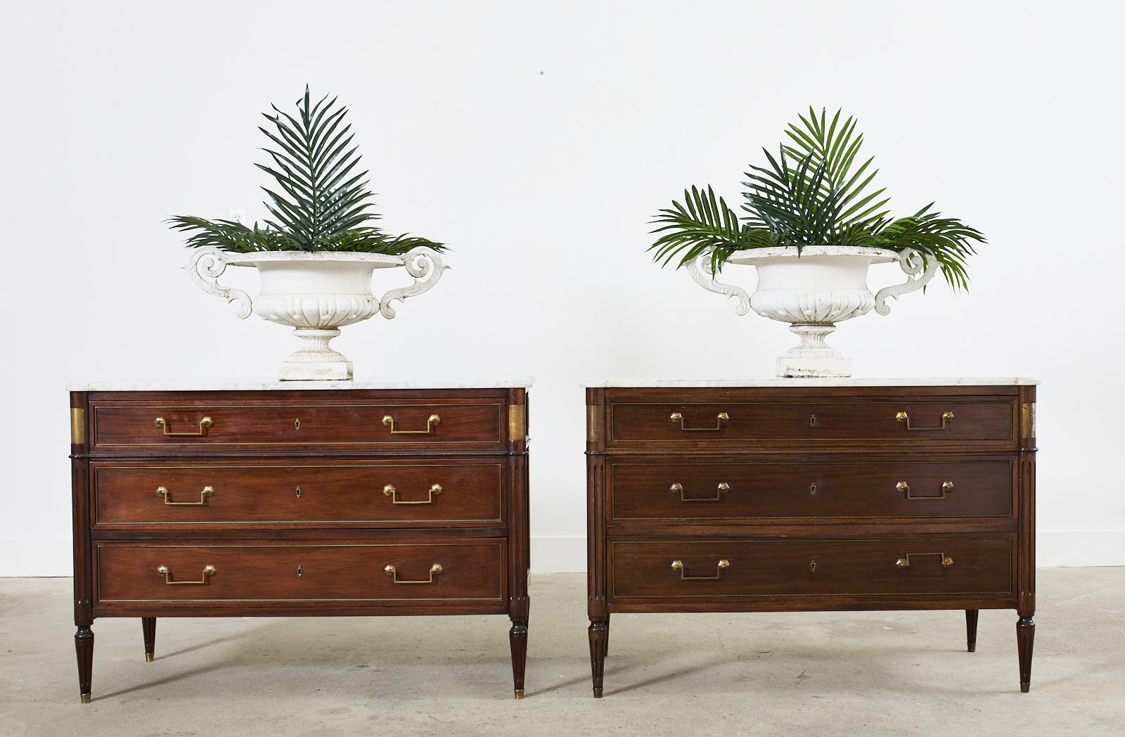 Opulent pair of French mahogany commodes or chest of drawers featuring stunning Italian Carrara marble tops. The cases are crafted in the grand neoclassical Louis XVI taste. Each case is fitted with three large storage drawers having brass border