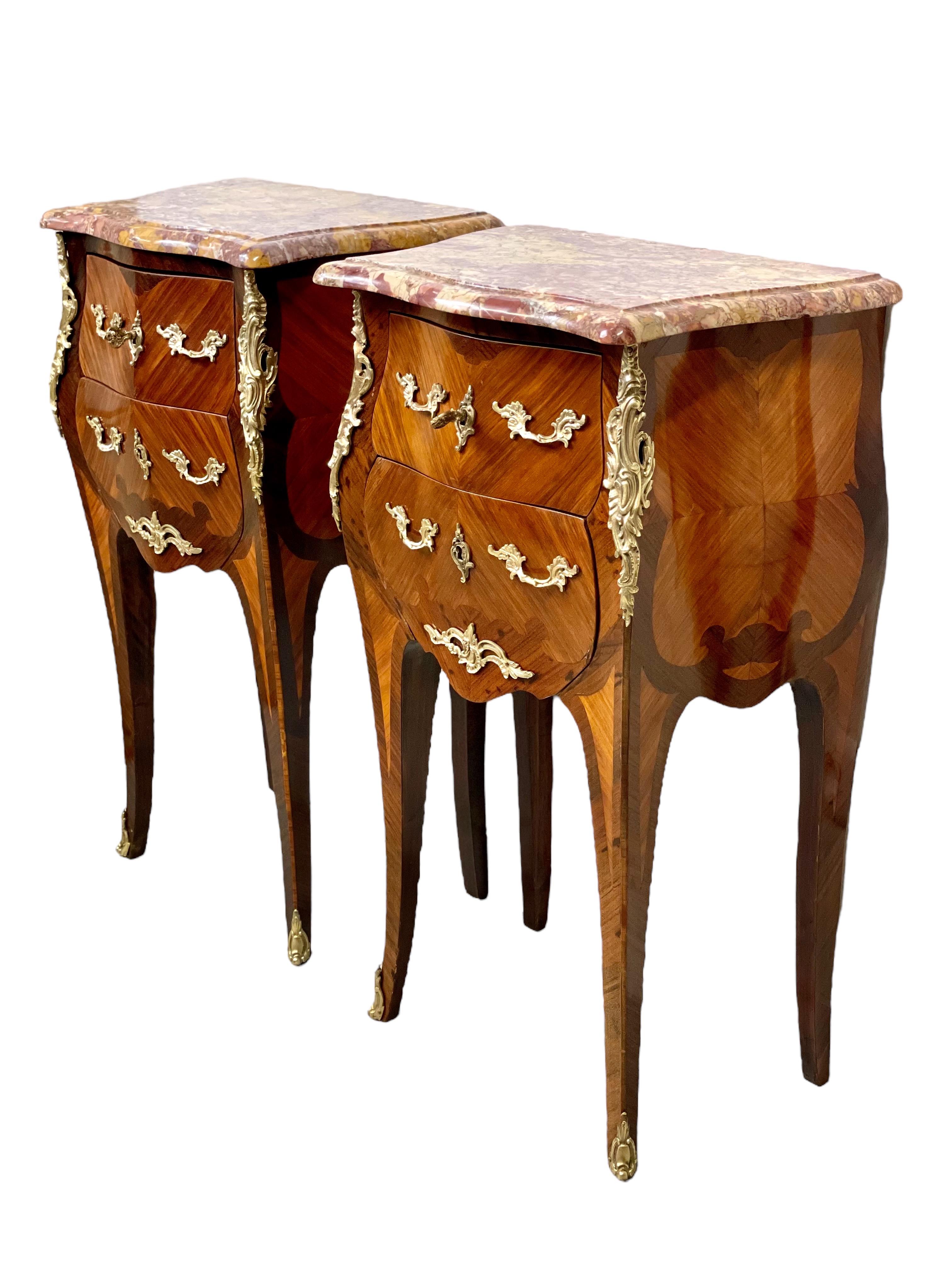 A wonderful pair of 19th century French marquetry petites commodes or bedside tables, finely crafted in the Louis XV style. Each one features two drawers, each fitted with fine gilt bronze scroll handles and escutcheons, and adorned in sophisticated