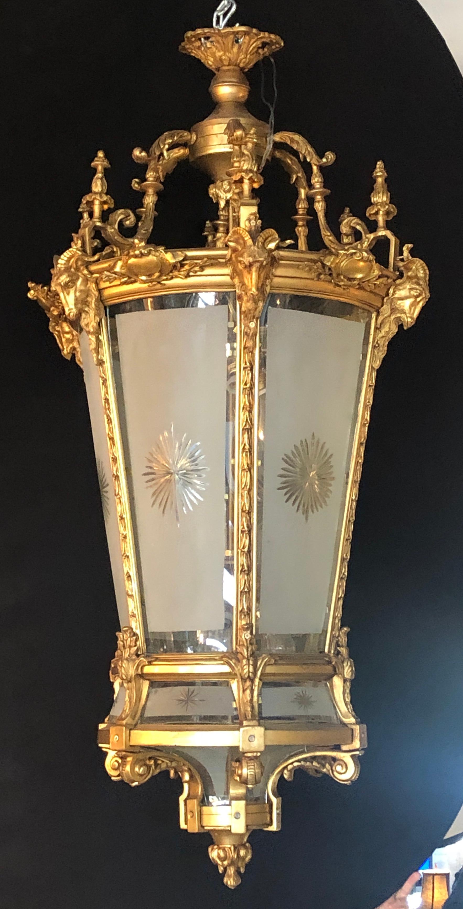 Pair of Louis XVI style monumental doré bronze ram's head etched glass lanterns. These spectacular one of a kind Lanterns are simply too stunning to behold. The frosted and etched star burst curved panels of glass framed in a heavy thick gilt gold
