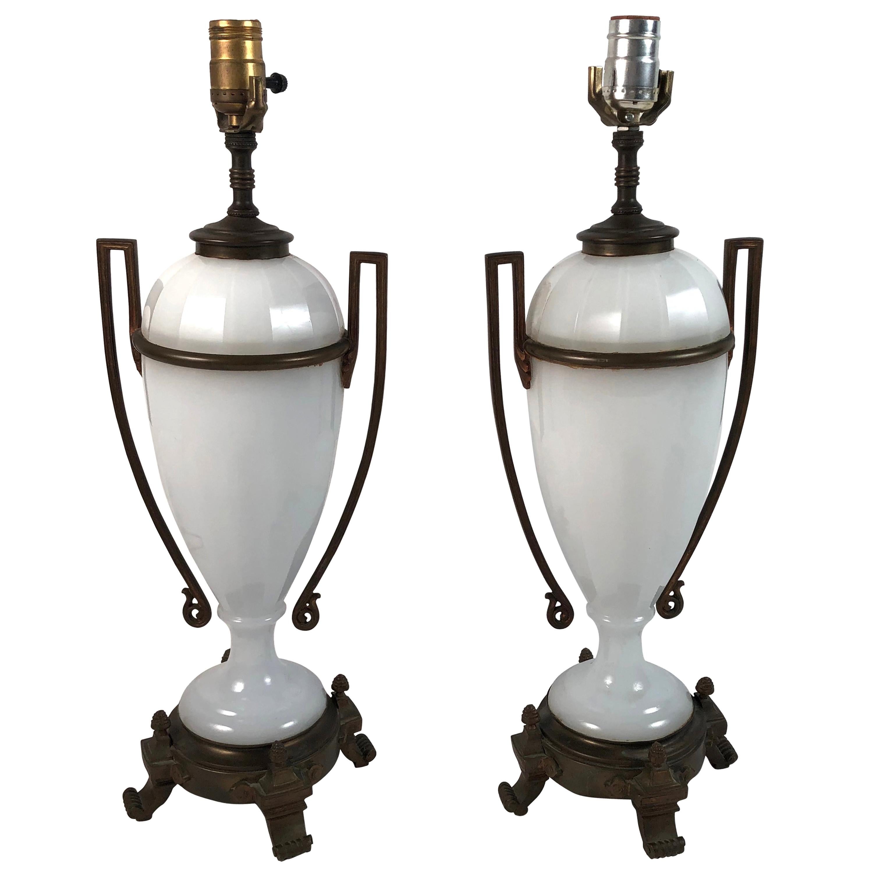 A pair of Louis XVI style neoclassical white opaline glass and ormolu lamps, each vase with stylized rectangular strap ormolu handles, the vases mounted on ormolu bases with pine cone finials. Newly re-wired. Shades shown for display only.

Base