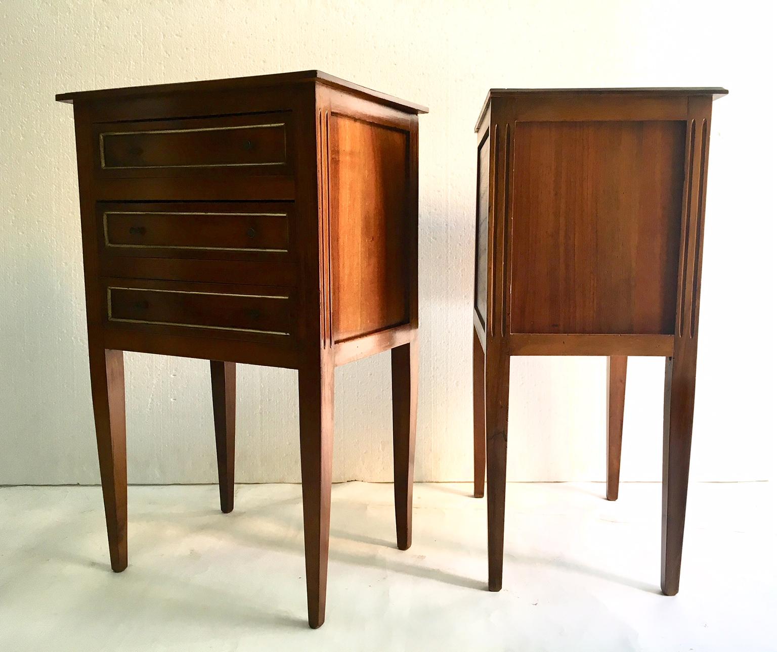 A late 20th century pair of walnut wood bedside tables or nightstands in the Louis XVI manner, each with three drawers with a simple brass fillet.