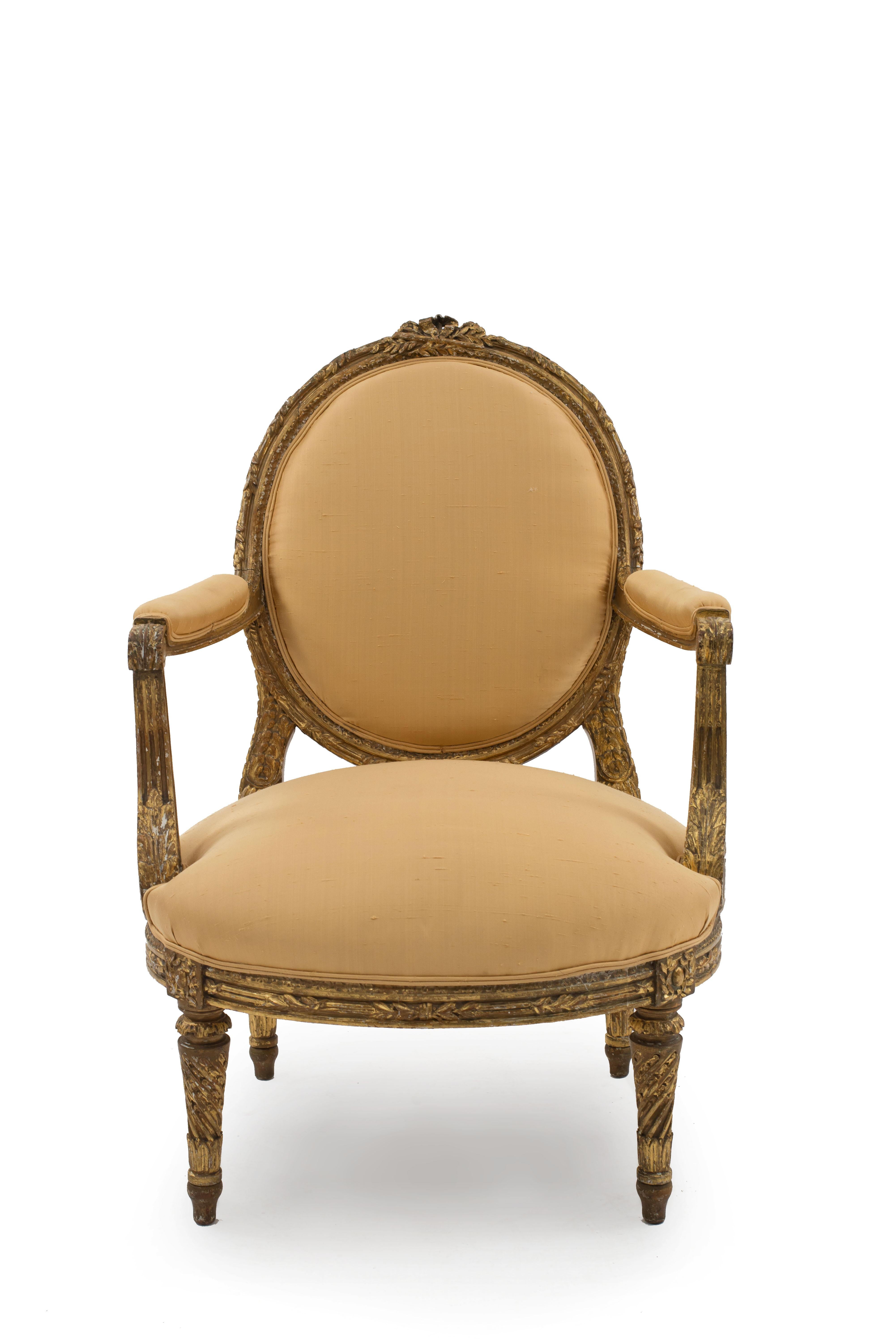 Pair of Louis XVI-style oval back armchairs with gold upholstery and carved giltwood frame and legs.