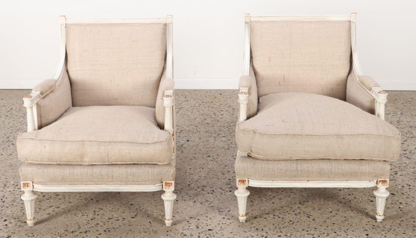 Pair of Louis XVI style painted and gilt bergere chairs C 1950. This pair of chairs was recently restored and upholstered in a burlap type fabric.