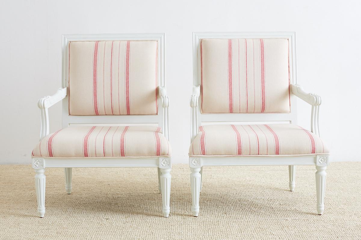 Whimsical pair of French Louis XVI style painted fauteuil armchairs featuring a white painted frame with a square seat and back. Supported by turned and fluted legs and upholstered in a light French red stripe fabric with a cream ground. Wide