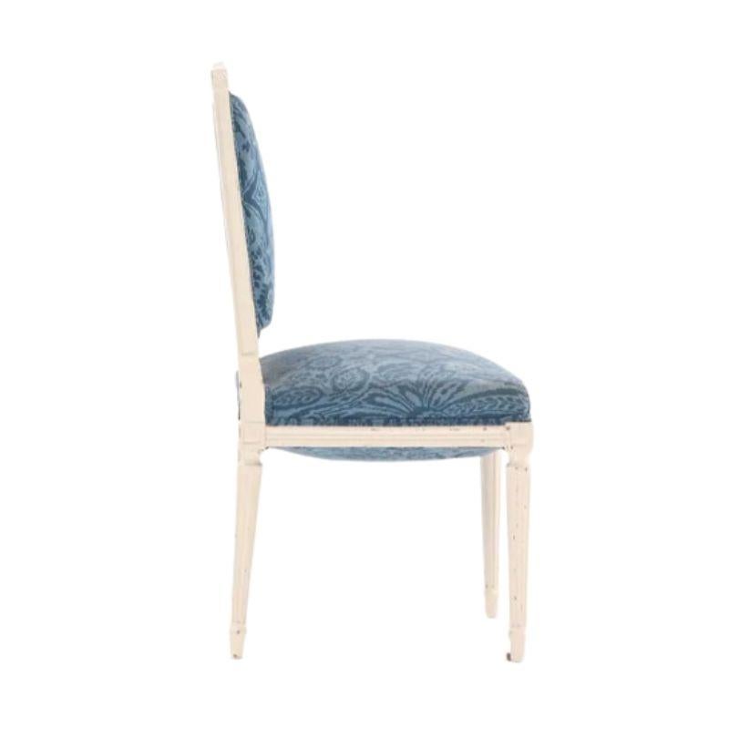 Paire de chaises d'appoint de style Louis XVI, peintes et tapissées, vers 1930. Sculptées et peintes en blanc, les chaises ont un dossier carré et des pieds cannelés. Les chaises sont revêtues d'un tissu damassé bleu dans un style intemporel et