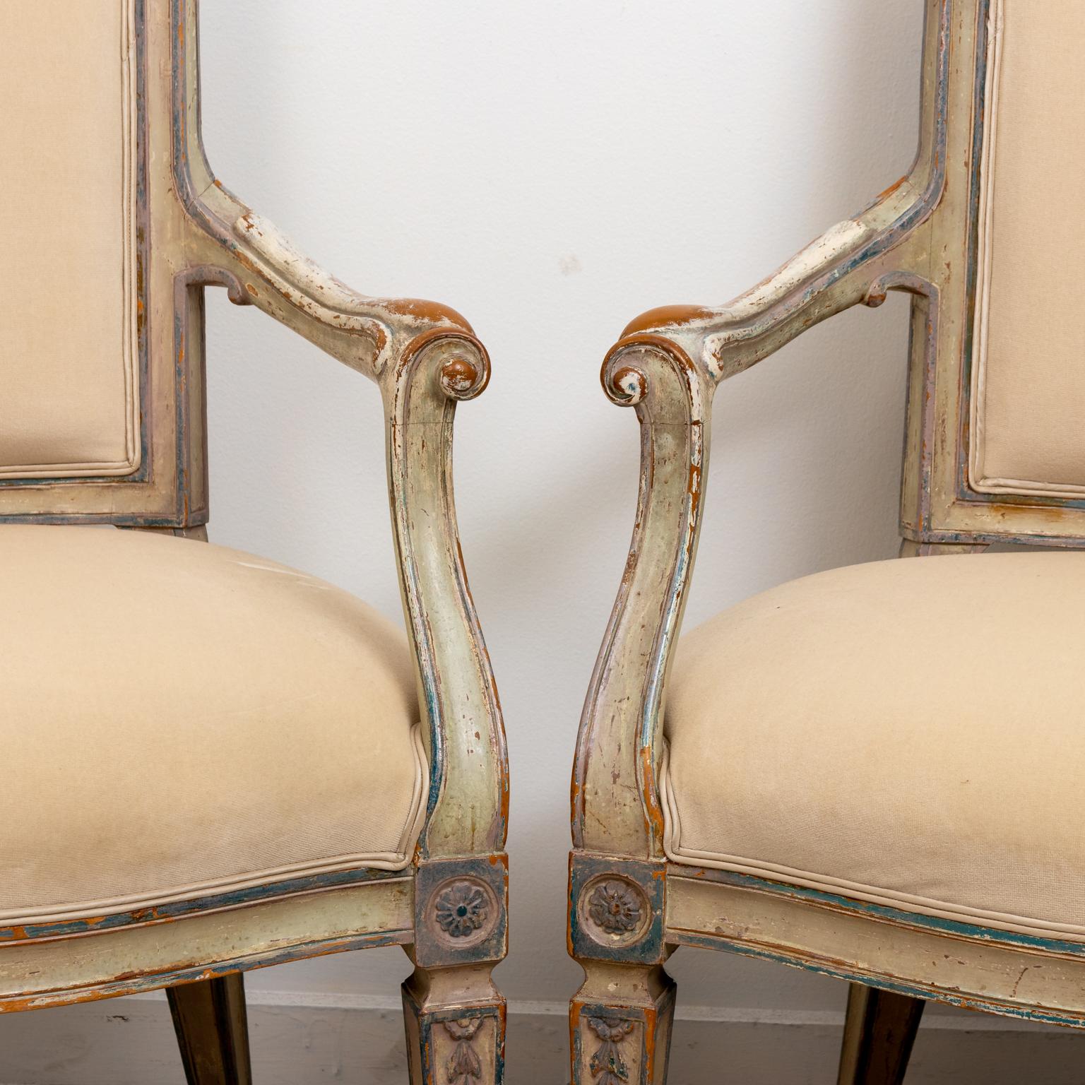 Pair of Louis XVI style painted and upholstered fauteuil armchairs with rectangular seat back, lattice print upholstered on the reverse side of the seat and turned legs ornamented with bellflower motifs. Please note of wear consistent age including