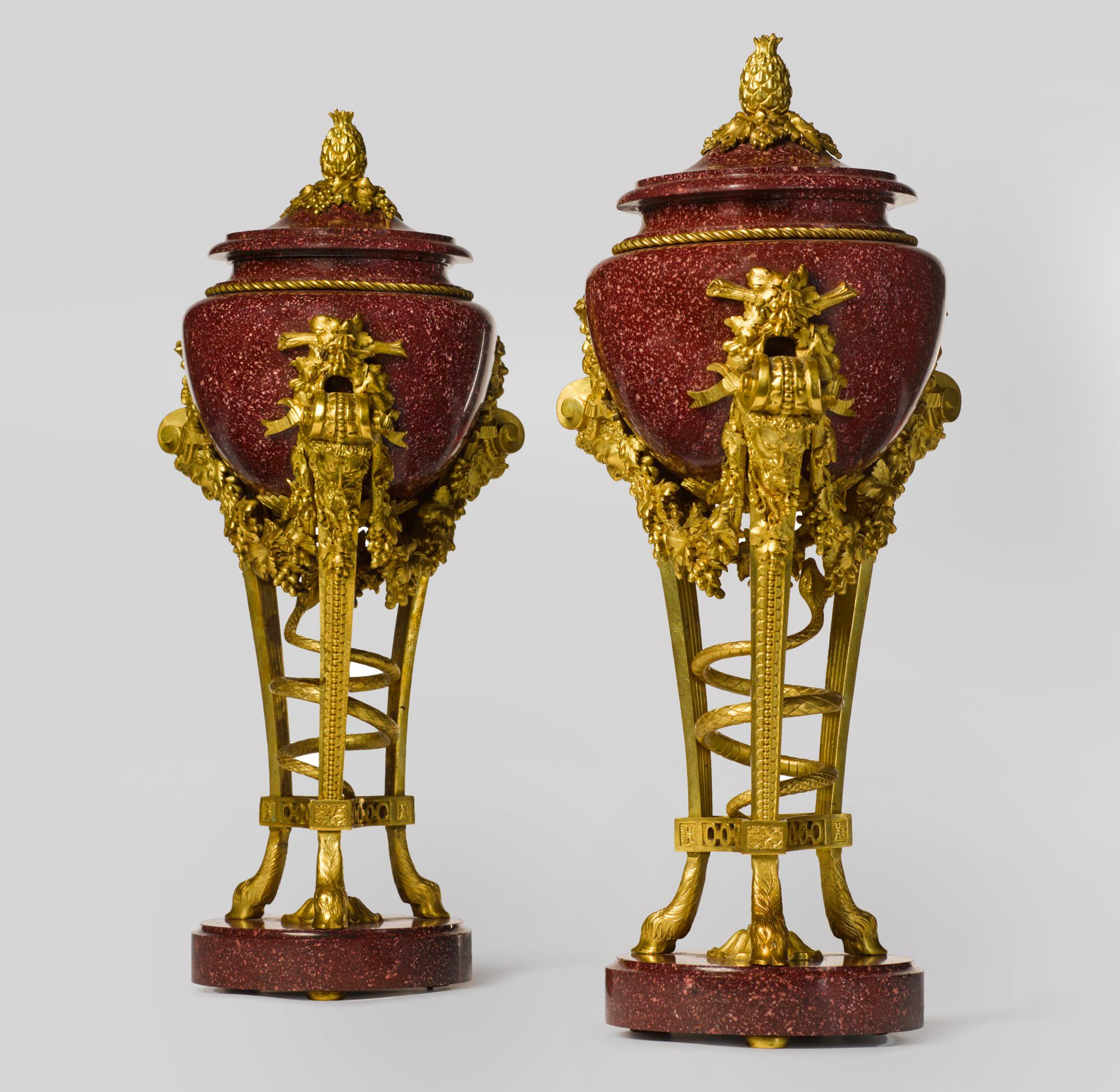 A pair of Louis XVI style gilt bronze mounted porphyry urns, after the Model by Pierre Gouthière.

Each urn is of neoclassical design, each with a circular base and a triform frame with a coiled snake in the center. The gilt bronze supports are