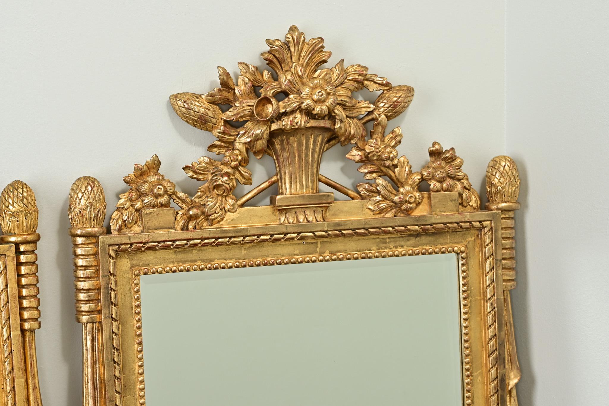 An impressive pair of reproduction gold gilt mirrors from Belgium. The frames are very decorative with crests of floral baskets and wheat. The new beveled mirror plates are surrounded with beading and other moldings typical of the Louis XVI style.