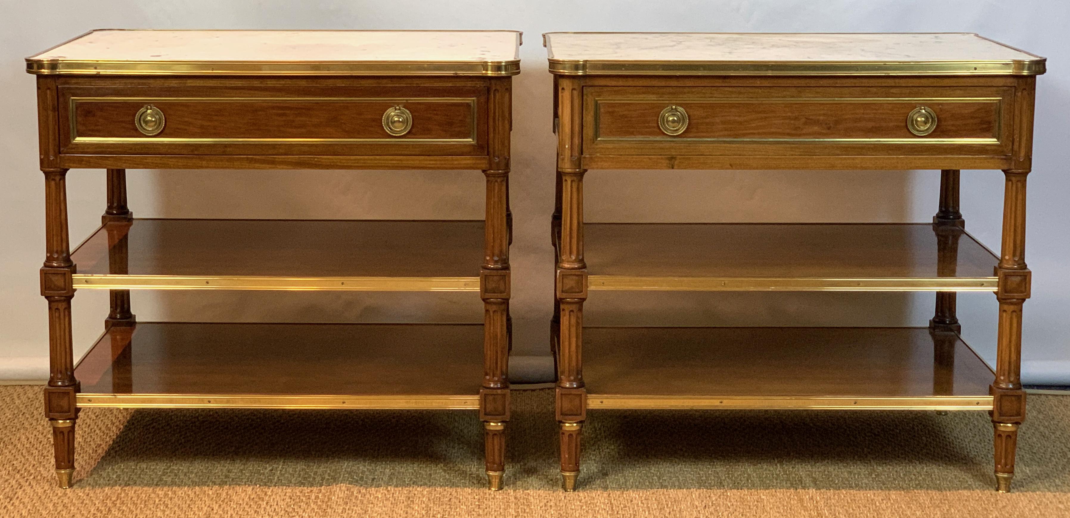 A magnificent pair of Louis XVI style carved mahogany side tables with inset white marble tops above a single drawer and two lower shelves accented with brass banding. The tables were made by Frederick P Victoria, noted New York antiques dealer,