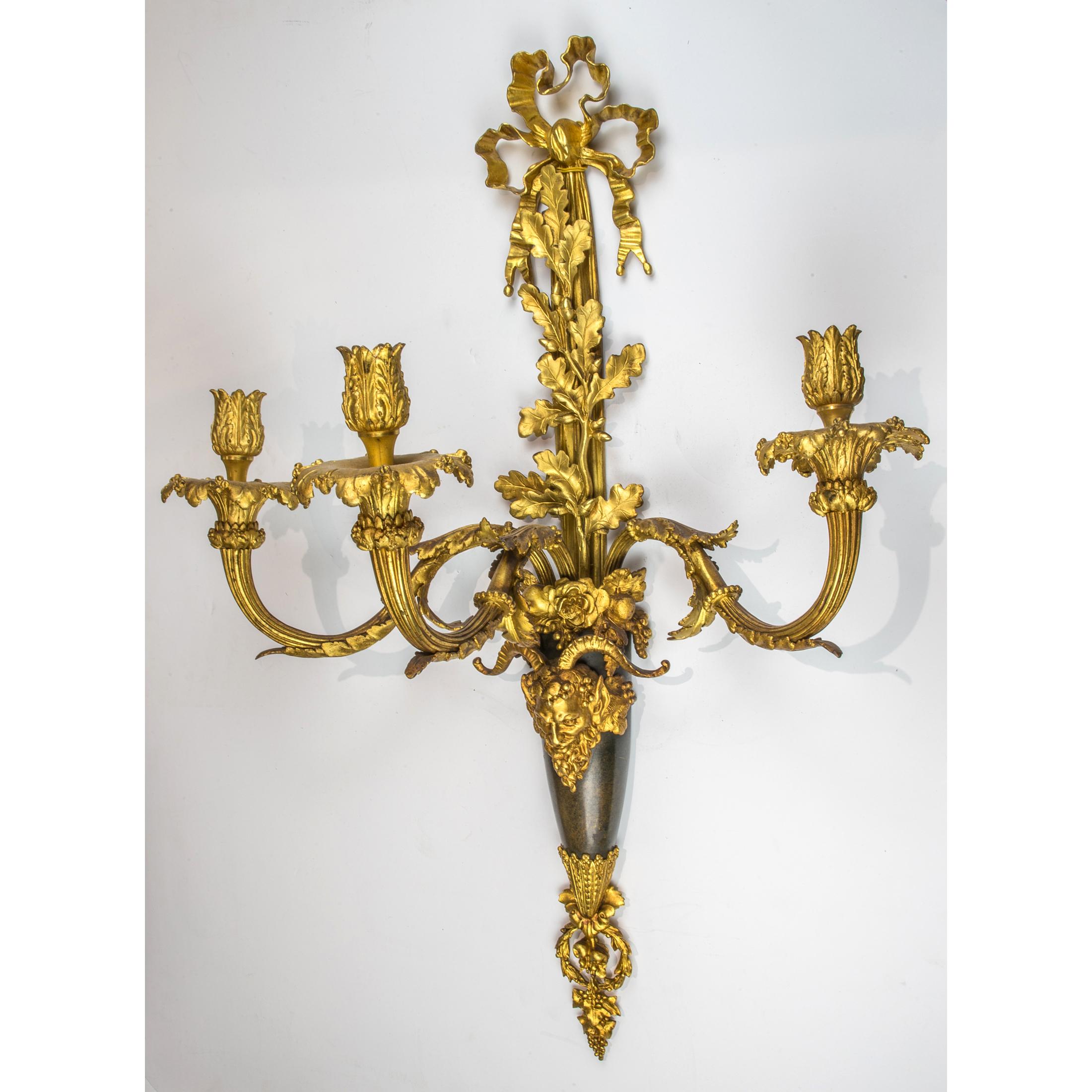 Exquisite quality pair of Louis XVI style three-light gilt and patinated bronze wall sconces. The backplate cast as a faisceau centered by a bacchiwc mask and issuing three scrolled acanthus and vine cast branches. 

Origin: French
Date: Late