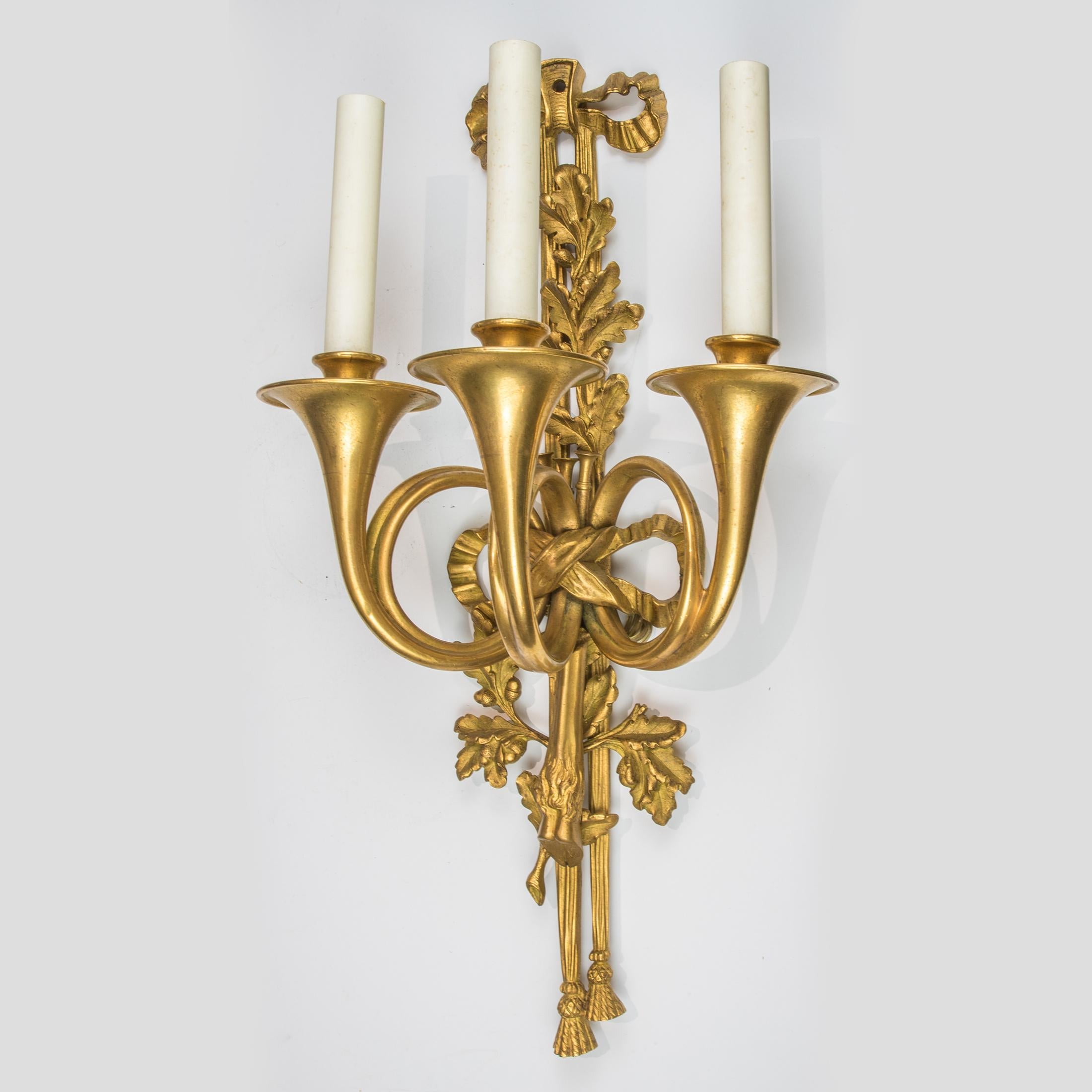 A symbolic and distinguished pair of Louis XVI-style ormolu three-light wall appliques. The tied drapery backplate molded with oak branches and stag hoofs and cast with tassel terminal. The three branches each, the form of a French hunting Horn.