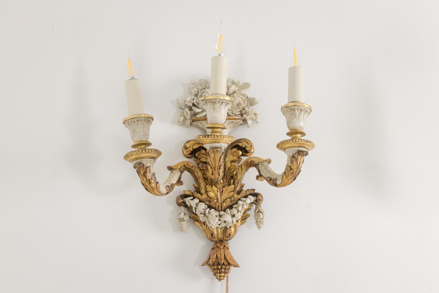 Coppia di applique in stile Luigi XVI in legno intagliato, dorato e laccato, con tre bracci di luce, decorati con un bouquet di fiori nella parte superiore e una ghirlanda di fiori.

Opera francese realizzata nel 1900 circa.

Dimensioni: H. H. 40 x