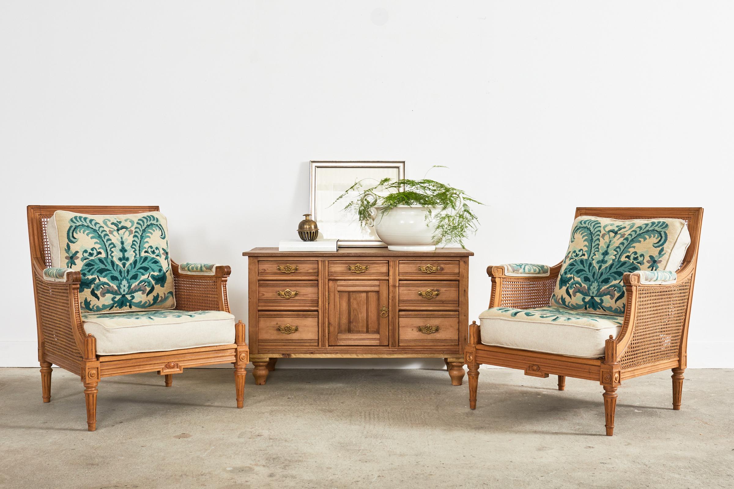Divine pair of French caned lounge chairs or armchairs featuring the original art nouveau style needlepoint. Beautifully crafted from walnut in the grand Louis XVI taste with a flat square back and seat. The seat and backs are caned and the sides