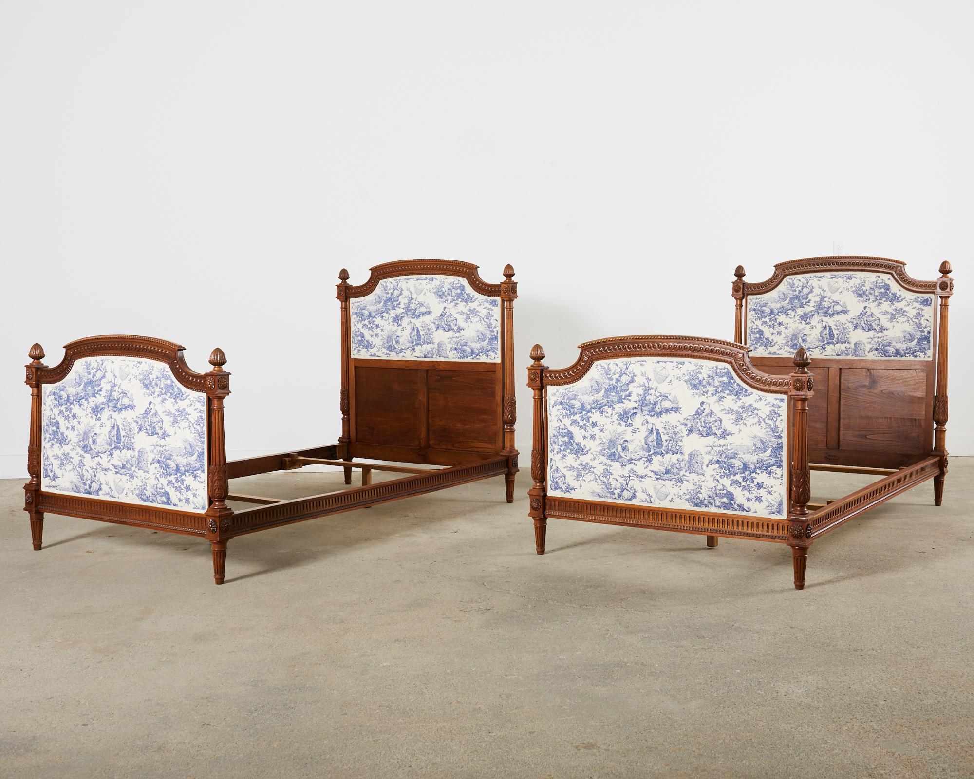 Remarkable pair of French walnut hand-carved beds featuring blue and white toile upholstery. Crafted in the grand neoclassical Louis XVI taste by Bardie in the Bordeaux region of France with makers branding stamp. The headboard and footboard have a