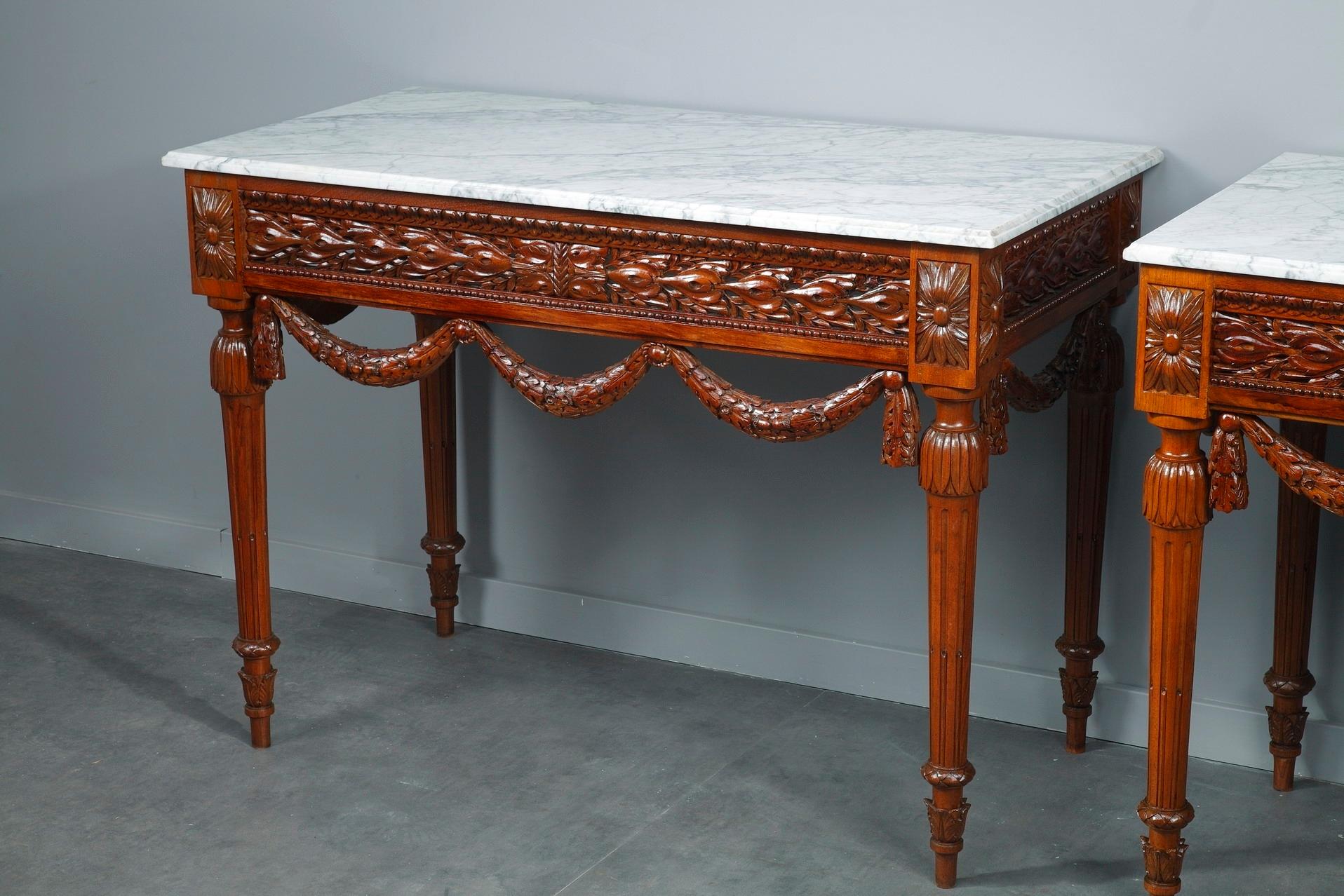 Pair of Louis XVI-style consoles tables crafted of walnut with white marble top. Crafted with a meticulous attention to detail, these tables epitomize the best elements of Louis XVI refined style: openwork foliage, garland of oak leaves and pearls.