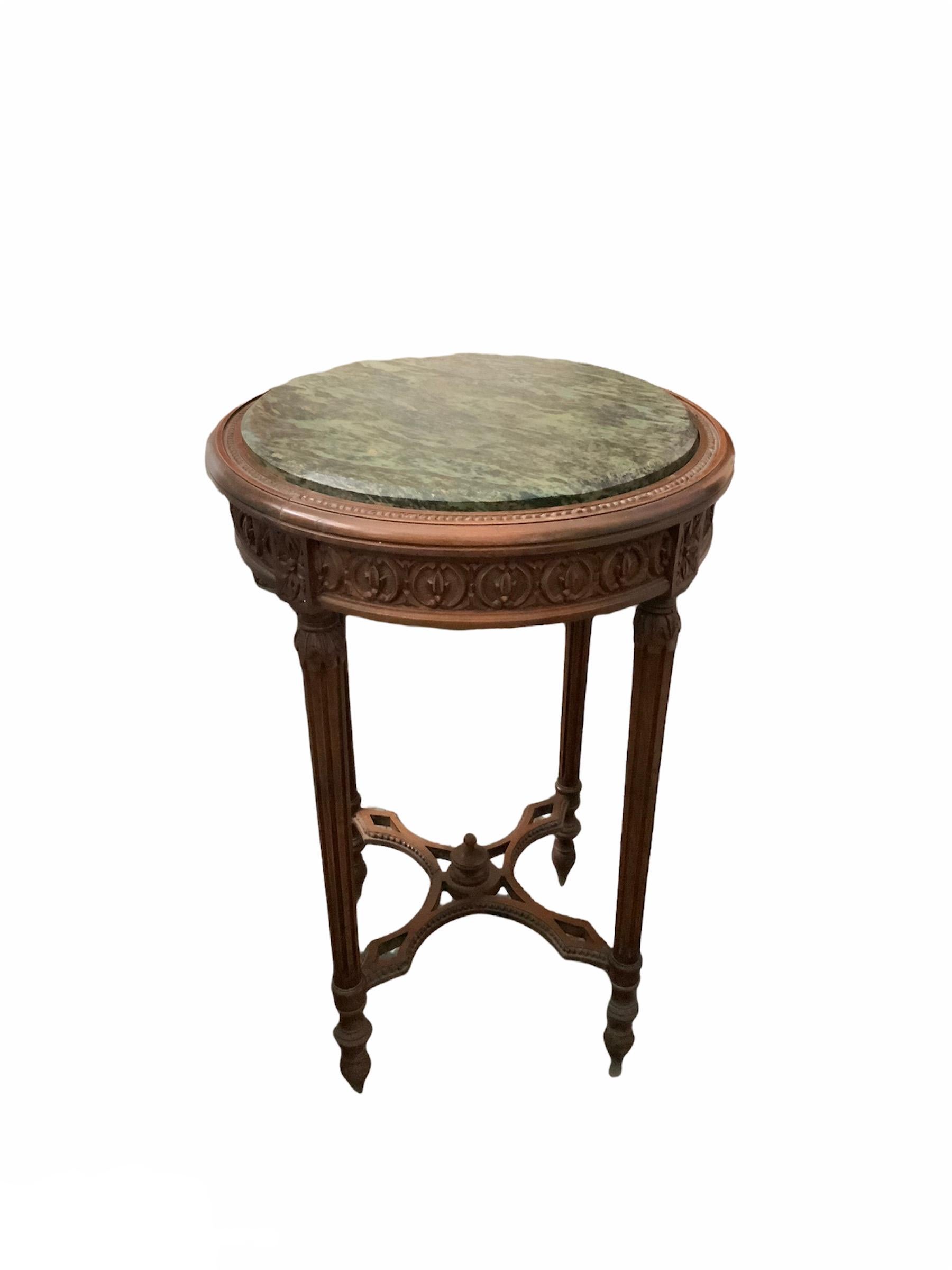 This is a pair of Louis XVI style wood side tables with marble tops. Both marble tops are green but different shades. They are round tables with four legs. Their legs are fluted and tapered. Their upper top is adorned with some kind of tobacco