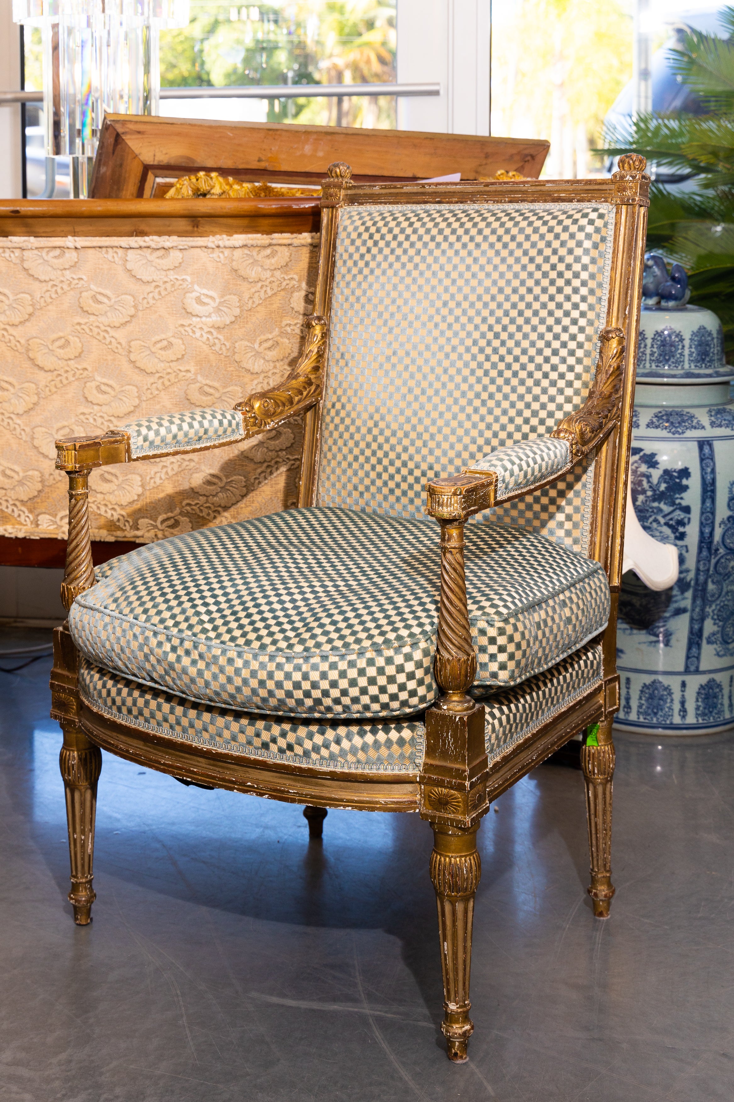 This is a French Louis XVI style gilt arm chair with square crest rail and out-scrolling arms, flanking upholstered back and seat with loose cushions. The chair is supported by round tapered fluted legs, 19th century.