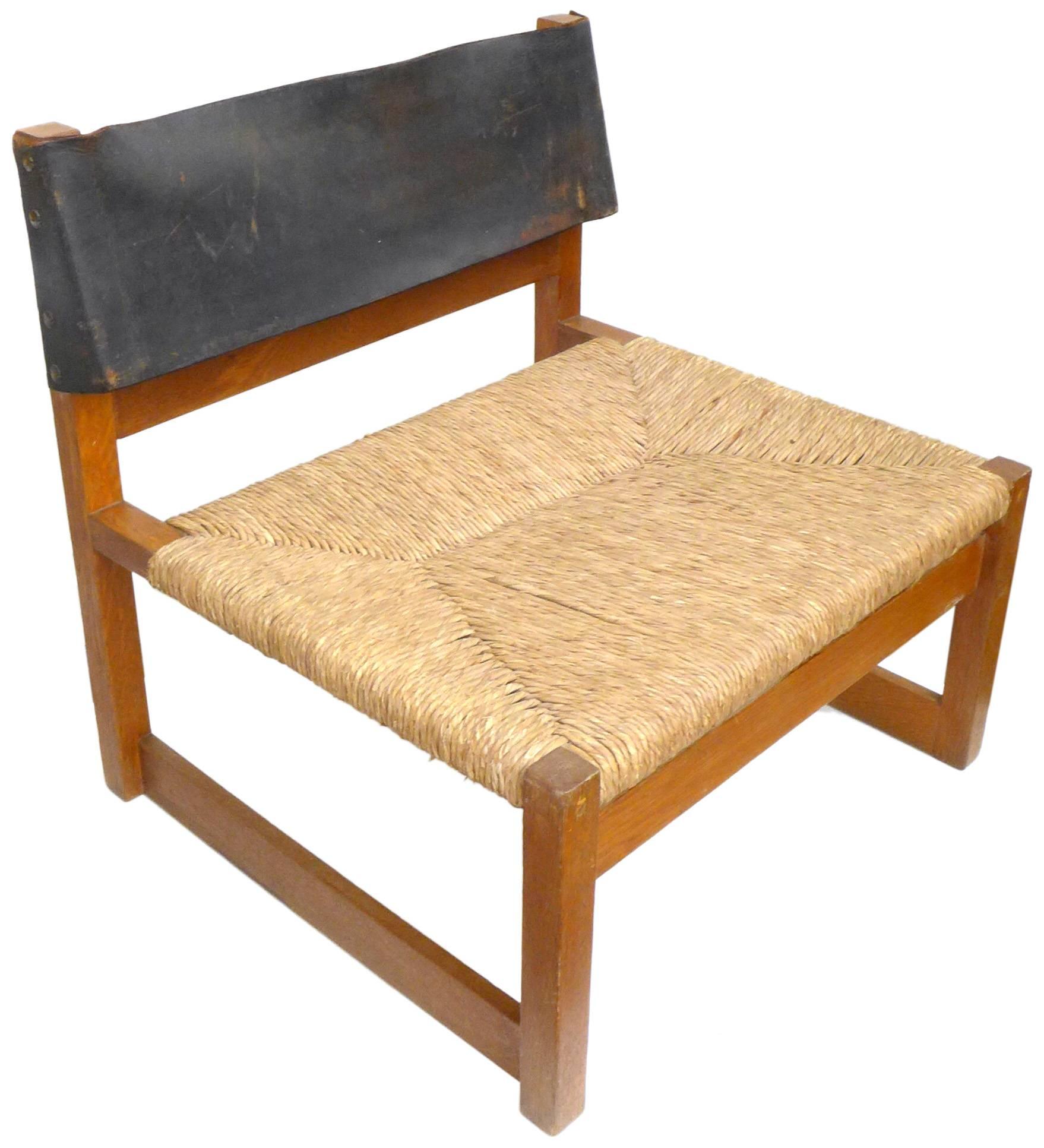 A handsome pair of lounge chairs by Spanish architect Javier Carvajal. A low, amply-proportioned, beautifully-joined wood frame with original, woven-rush seat and leather-strap back. Alluring form and mix of materials with great patina from age.
