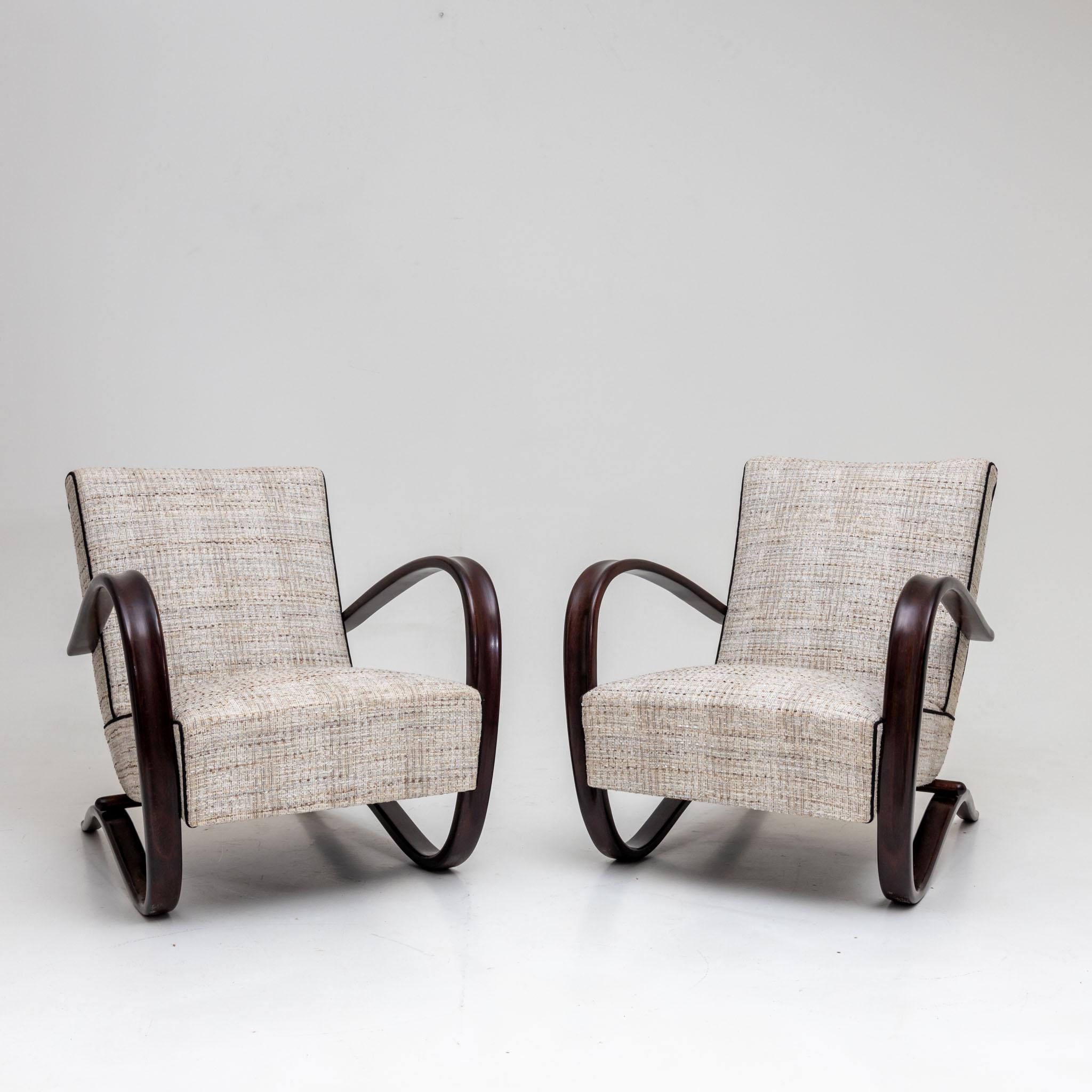 Pair of Halabala armchairs with gray-beige mottled upholstery. The dark stained armrests run in an elegant c-shaped sweep around the side of the seat cushion and become the supporting frame. The chairs have been newly upholstered in a high quality
