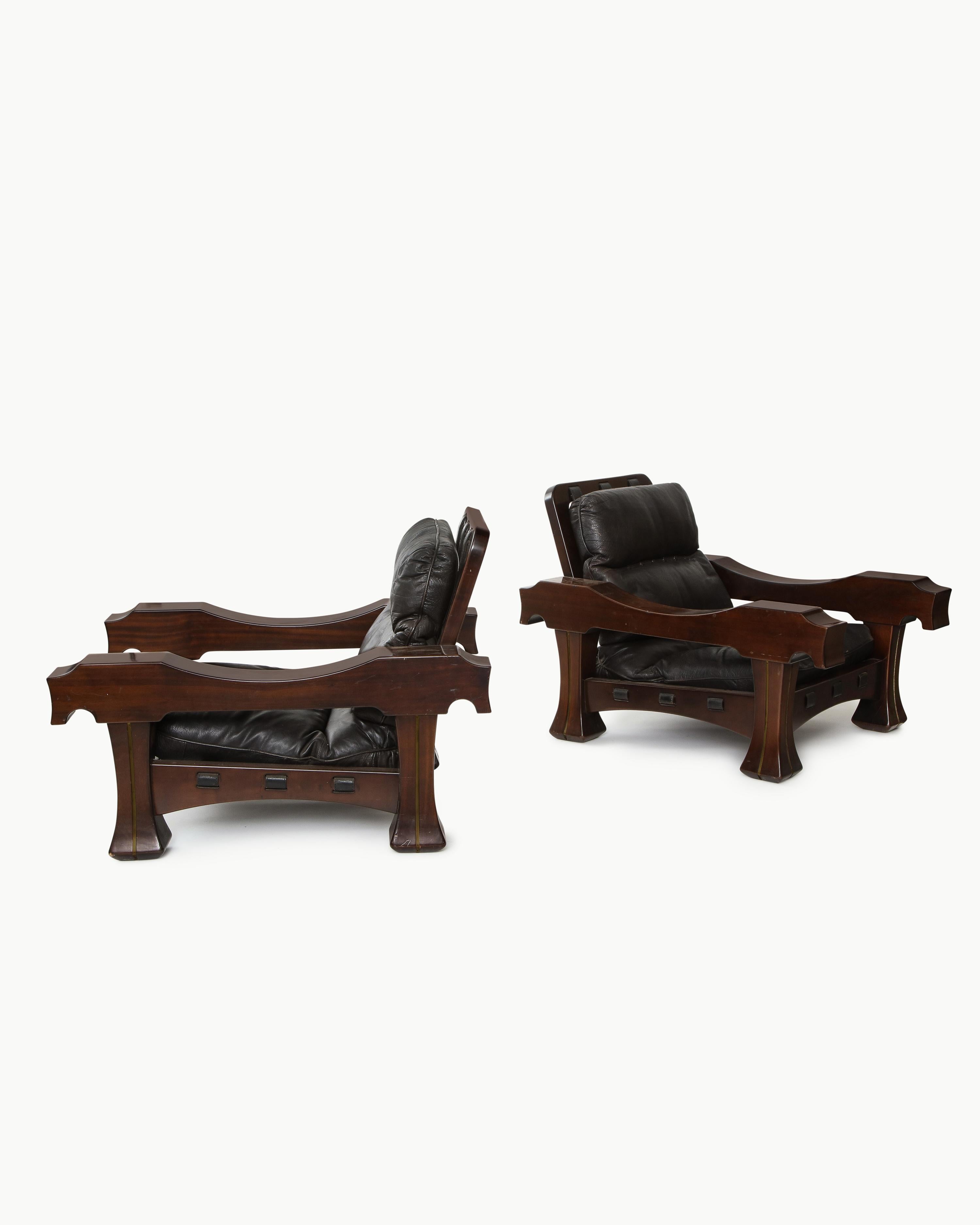 Massive pair of Ussaro armchairs by Luciano Frigerio in tropical wood, black leather and brass. These chairs embody the solid and sturdy masculine style emblematic of Frigerio's designs. The mixed media construction of these unique models enhance